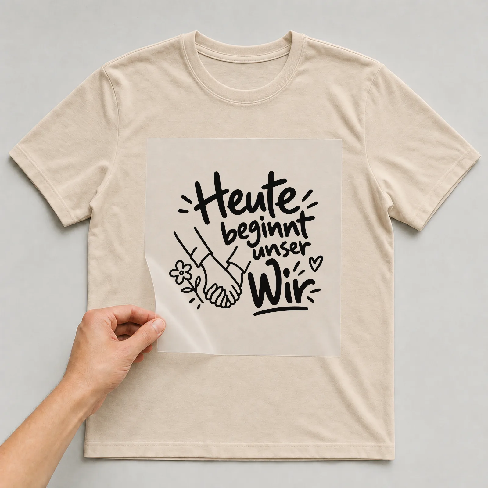 Bügelbild „Heute beginnt unser Wir“ auf beigem T-Shirt, Folie wird aufgelegt