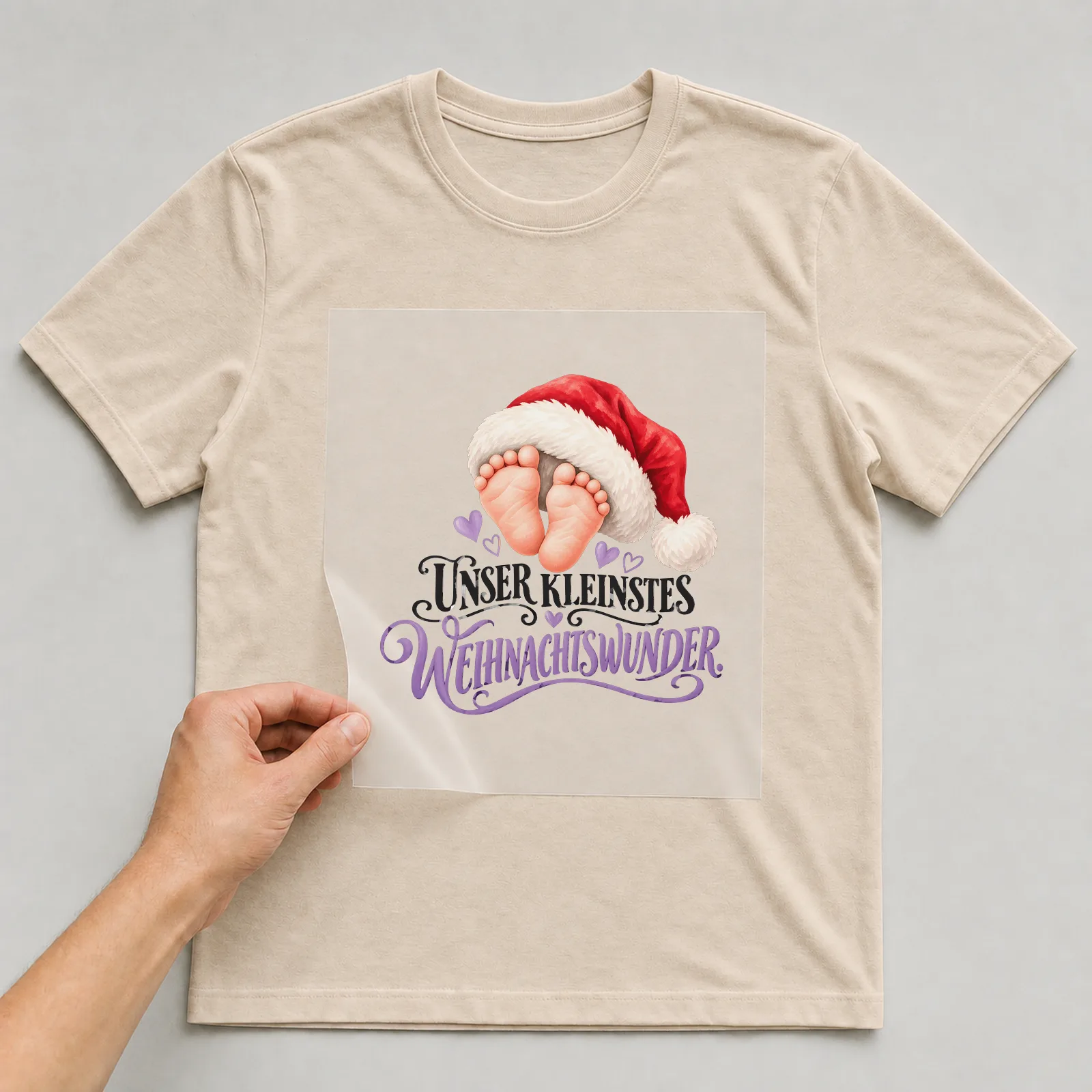Bügelbild „Unser kleinstes Weihnachtswunder“ auf beigem T-Shirt, Folie wird aufgelegt
