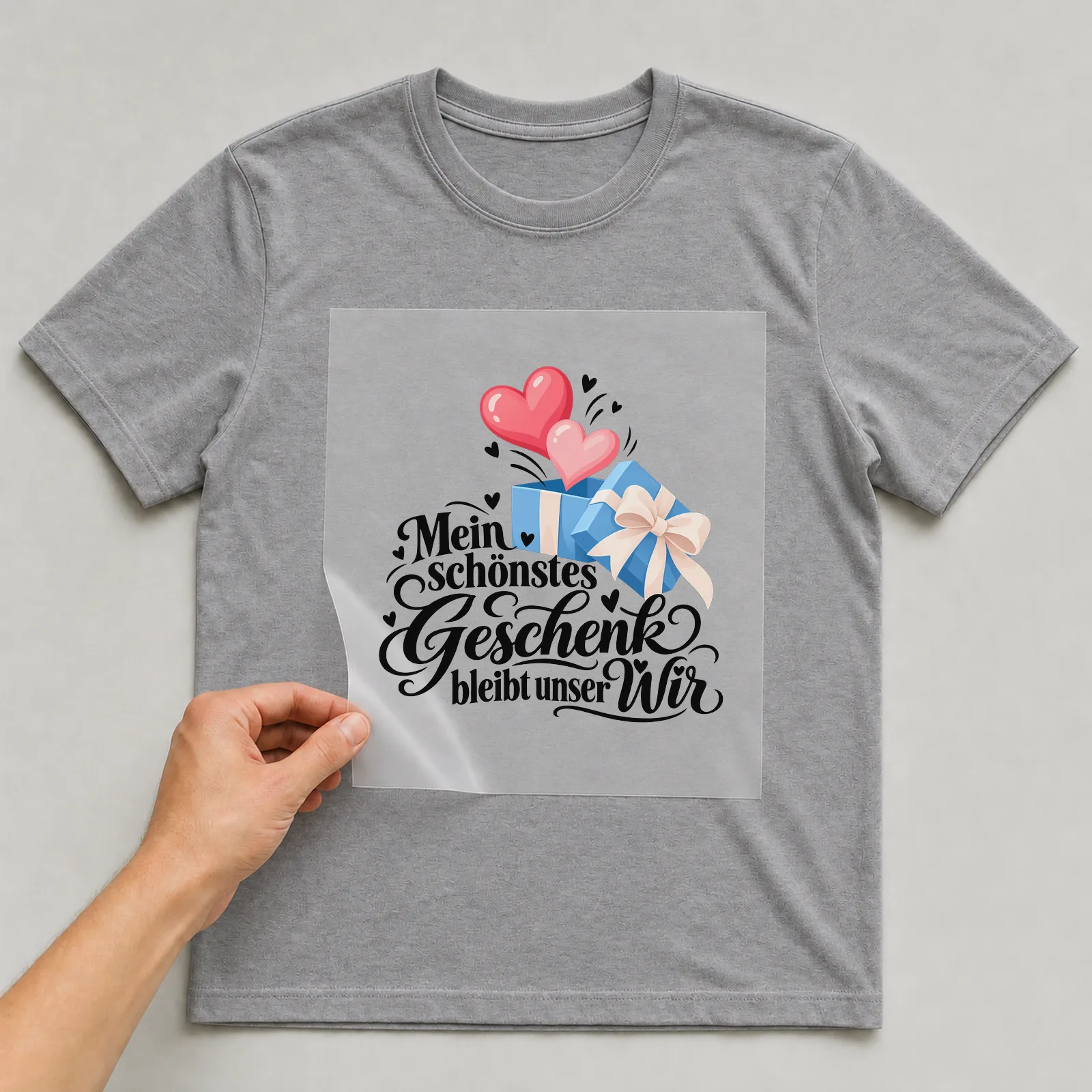 Bügelbild „Mein schönstes Geschenk bleibt unser Wir“ auf grauem T-Shirt, Folie wird aufgelegt