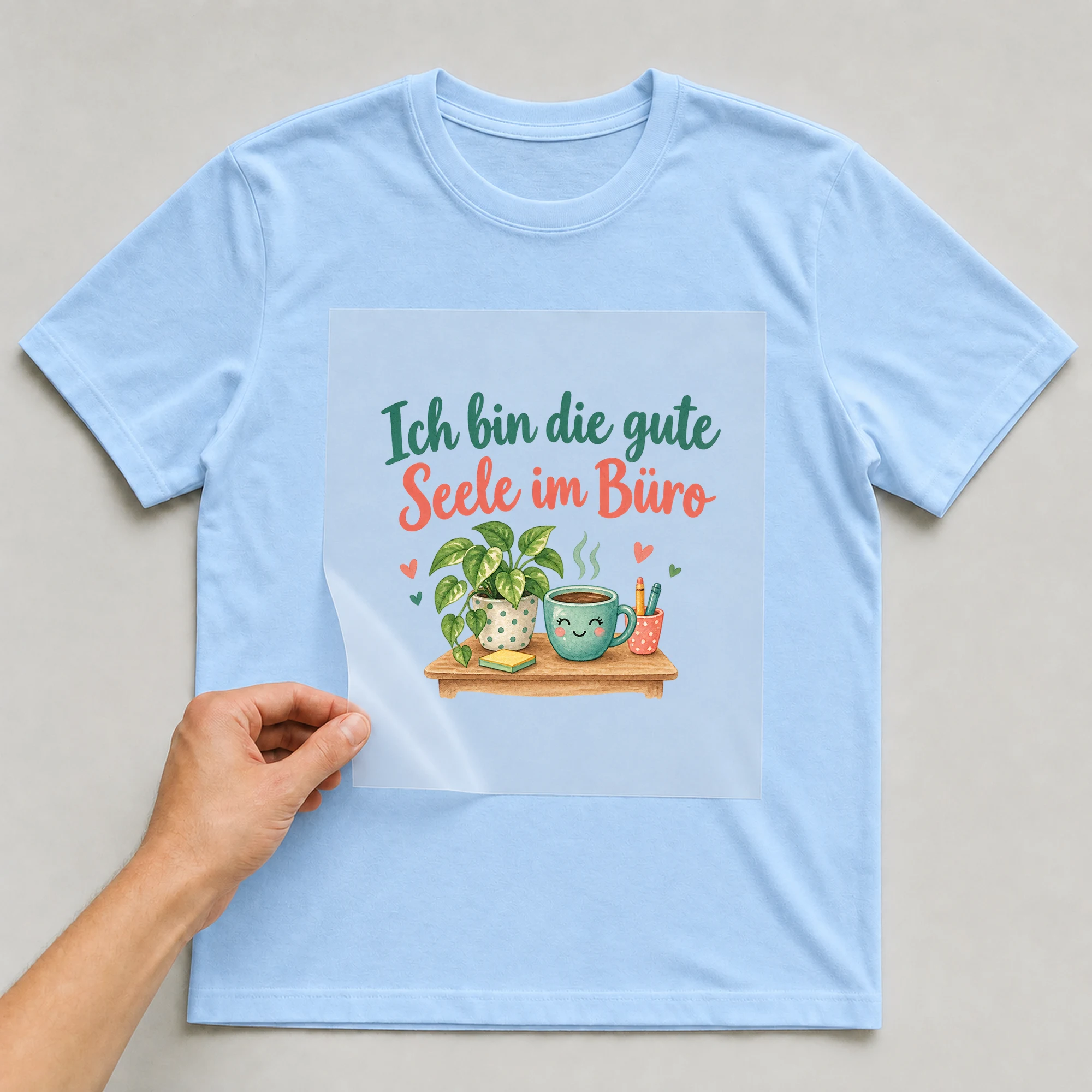 Bügelbild „Ich bin die gute Seele im Büro“ auf babyblauem T-Shirt, Folie wird aufgelegt