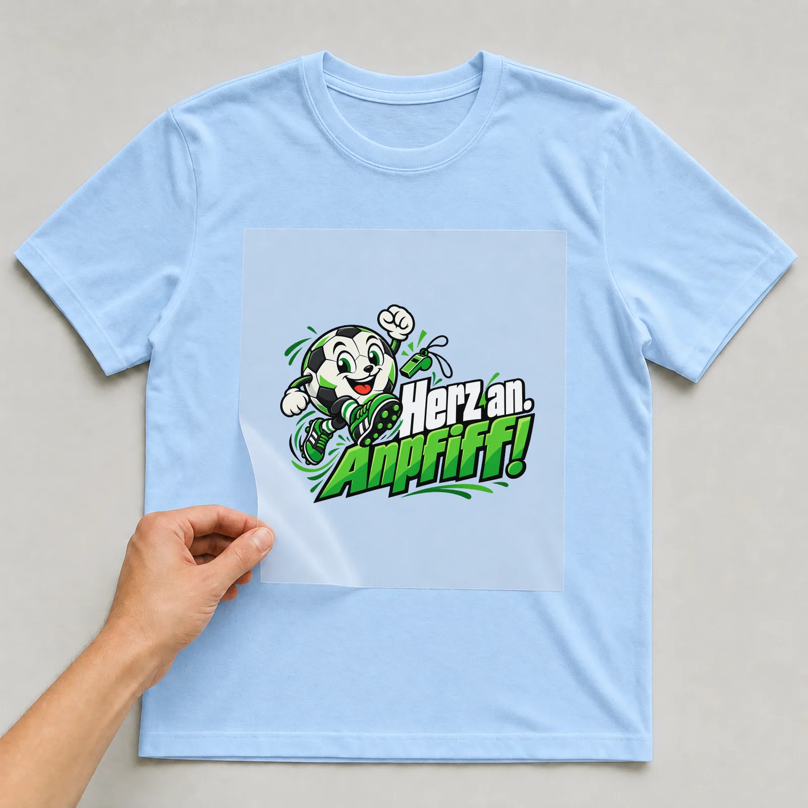 Bügelbild „Herz an. Anpfiff!“ auf hellblauem T-Shirt, Folie wird aufgelegt