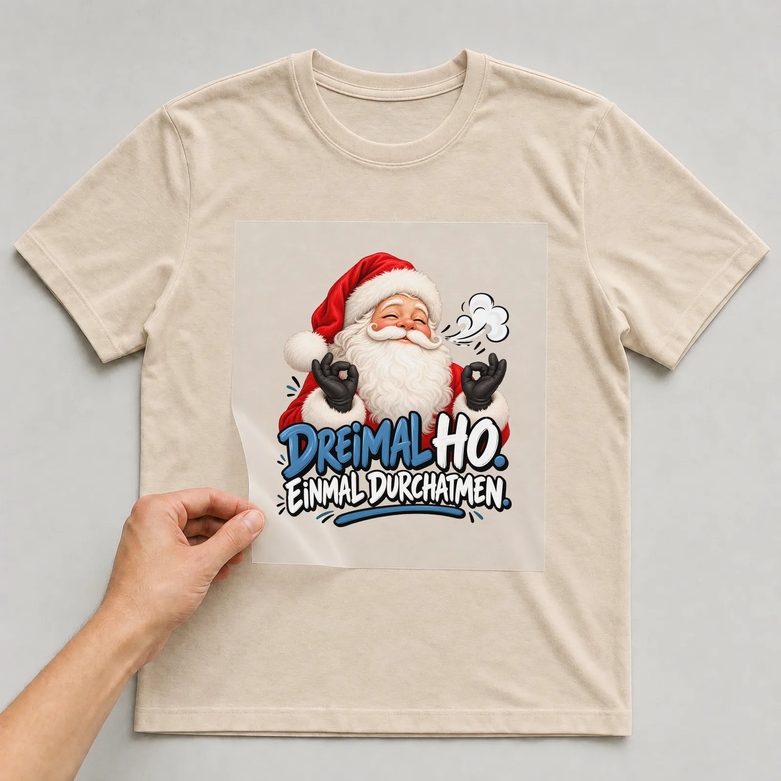 Bügelbild „Dreimal Ho. Einmal durchatmen.“ auf beigem T-Shirt, Folie wird aufgelegt