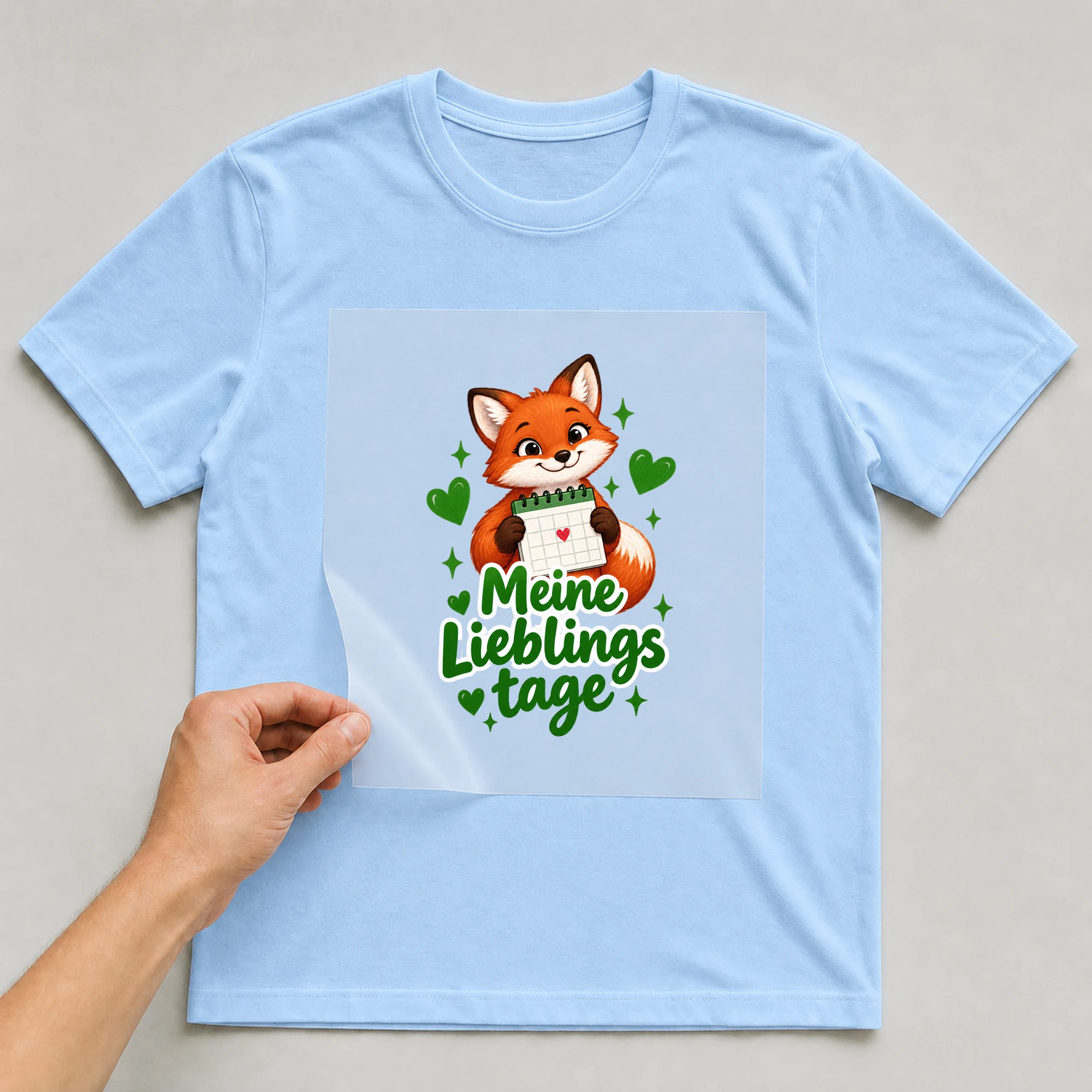 Bügelbild „Meine Lieblingstage“ auf babyblauem T-Shirt, Folie wird aufgelegt