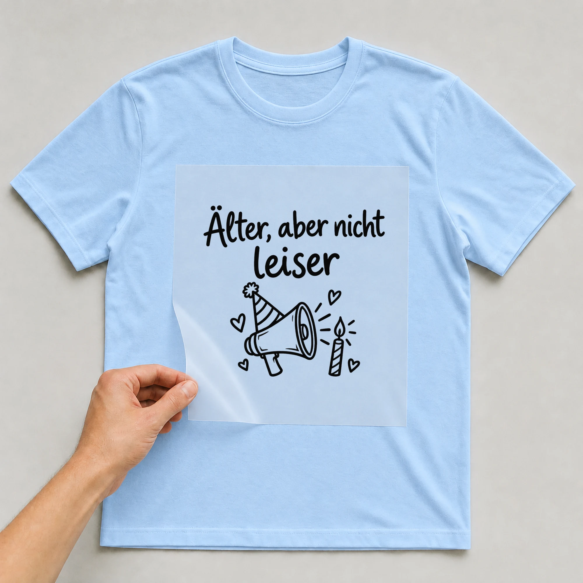 Bügelbild „Älter, aber nicht leiser“ auf babyblauem T-Shirt, Folie wird aufgelegt