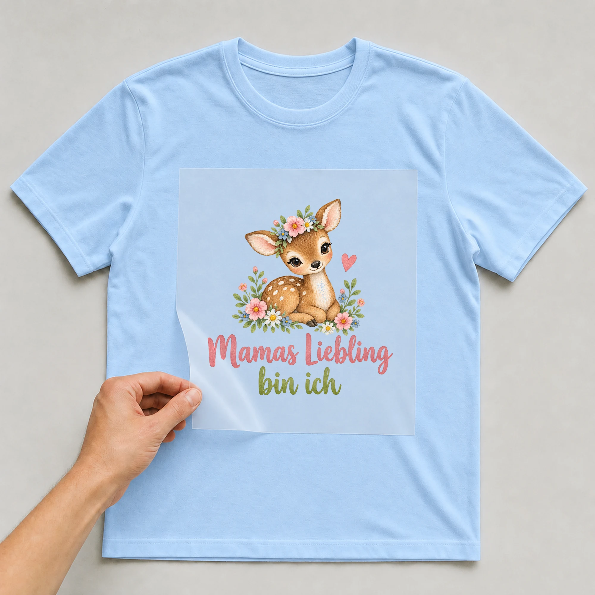 Bügelbild „Mamas Liebling bin ich“ auf babyblauem T-Shirt, Folie wird aufgelegt