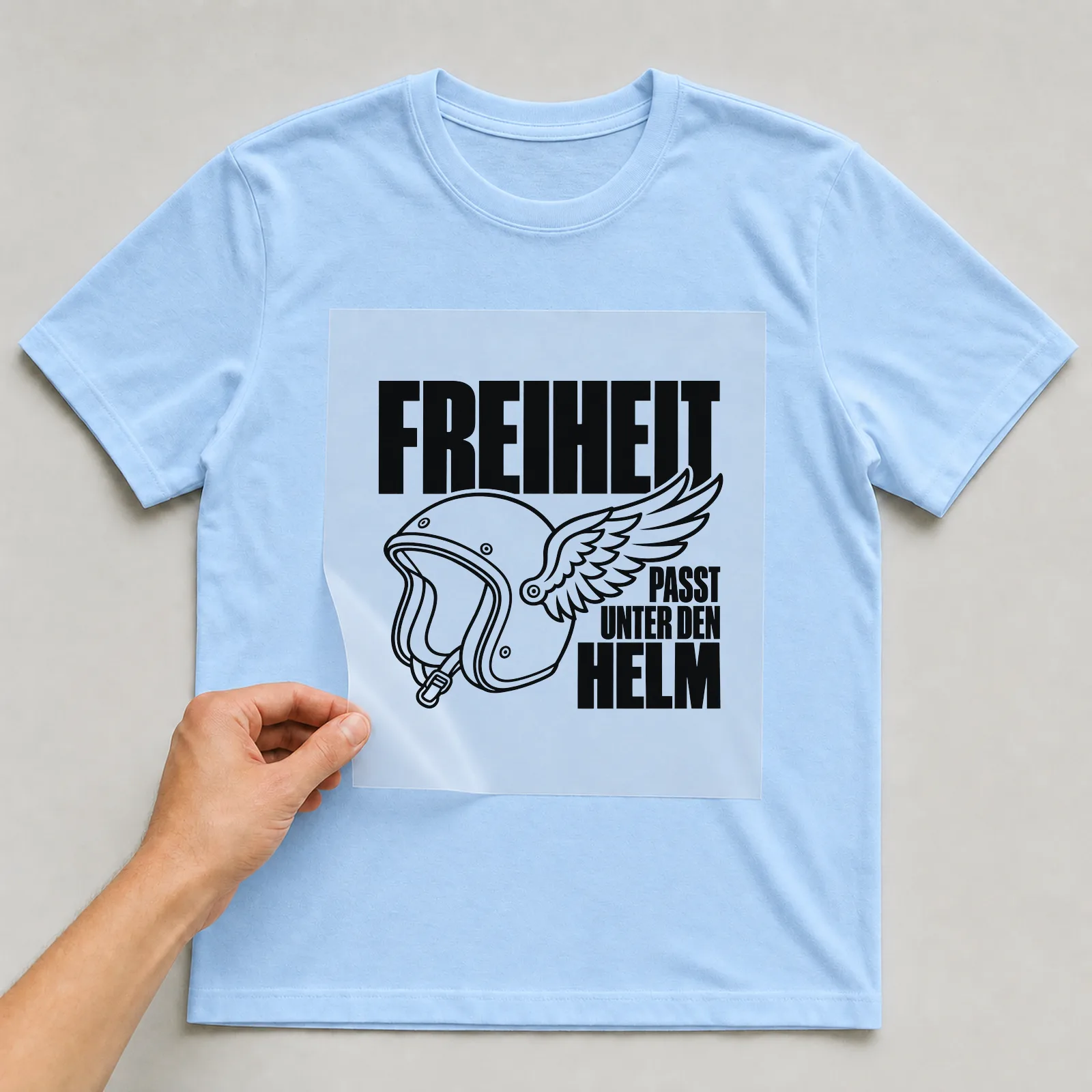 Bügelbild „Freiheit passt unter den Helm“ auf hellblauem T-Shirt, Folie wird aufgelegt