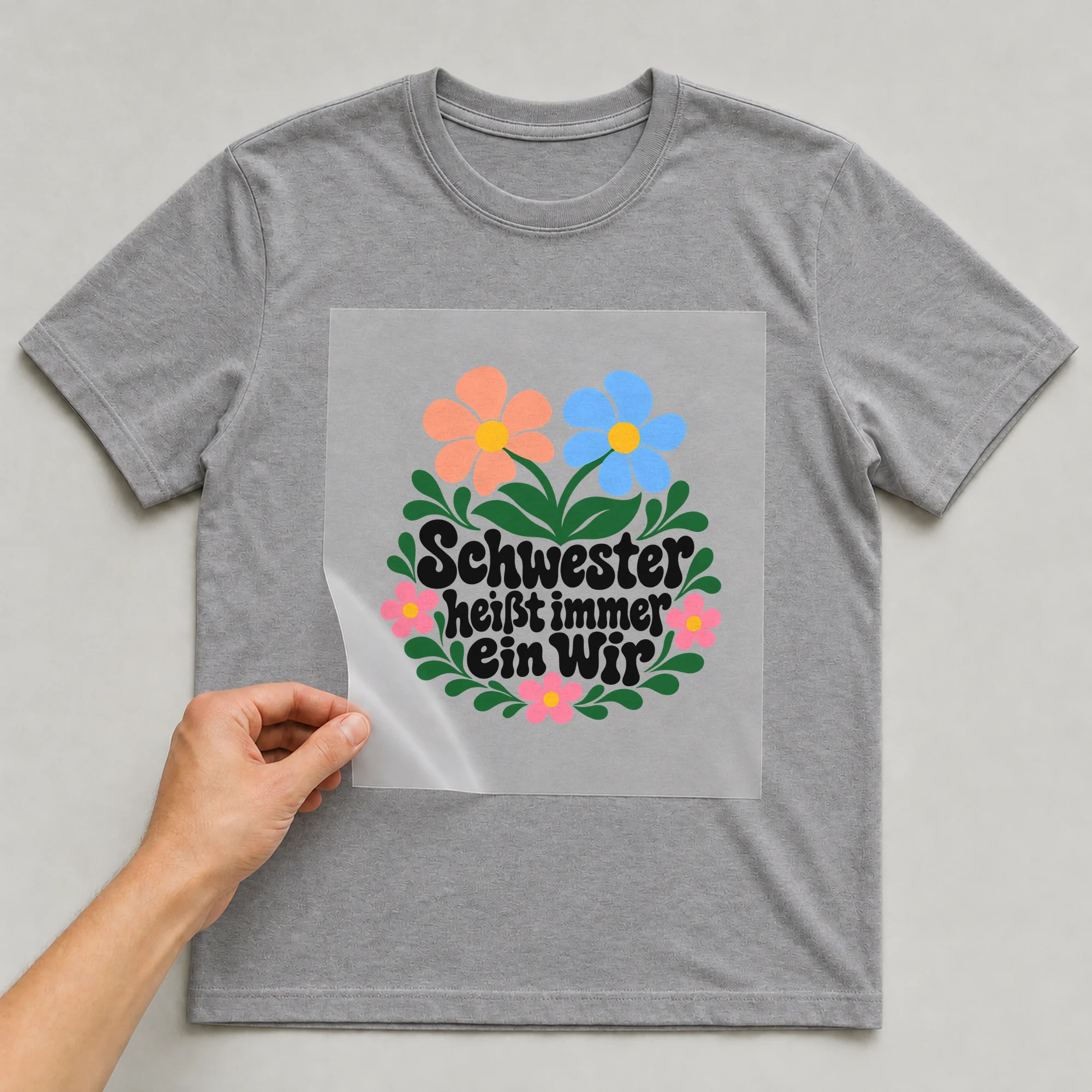 Bügelbild „Schwester heißt immer ein Wir“ auf grauem T-Shirt, Folie wird aufgelegt