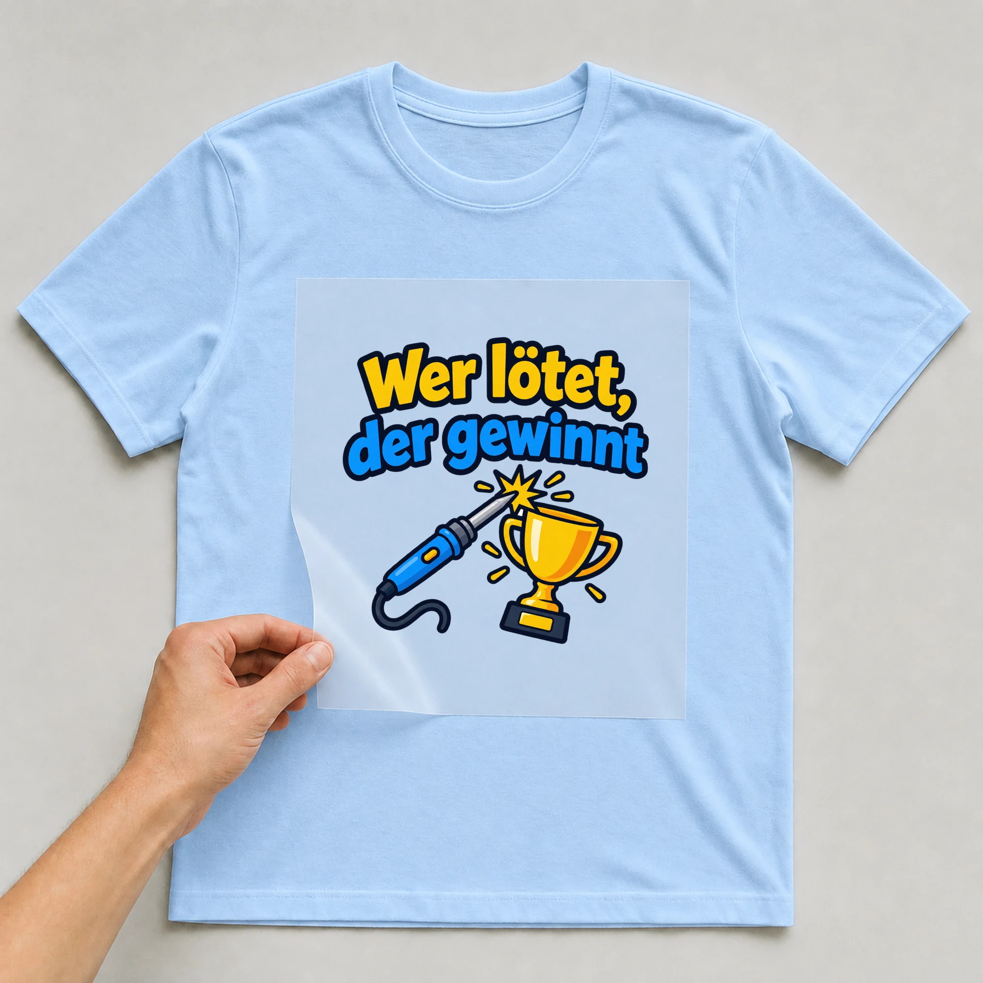 Bügelbild „Wer lötet, der gewinnt“ auf babyblauem T-Shirt, Folie wird aufgelegt