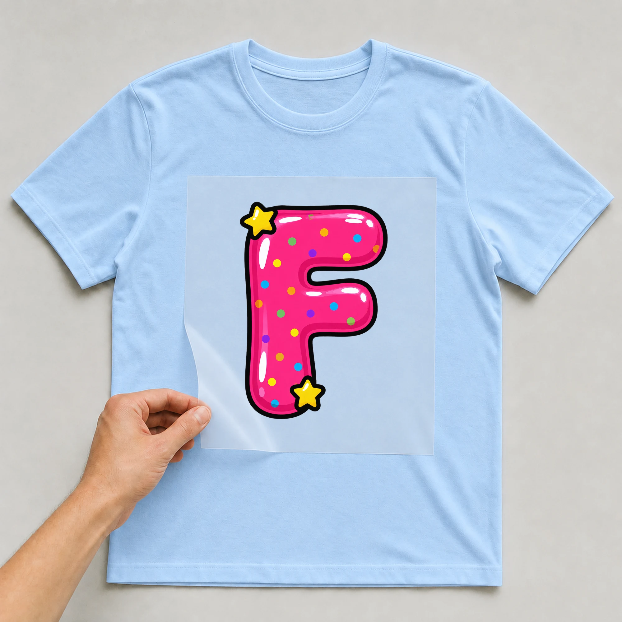 Bügelbild „Buchstabe F im Comic-Ballon-Stil“ auf babyblauem T-Shirt, Folie wird aufgelegt