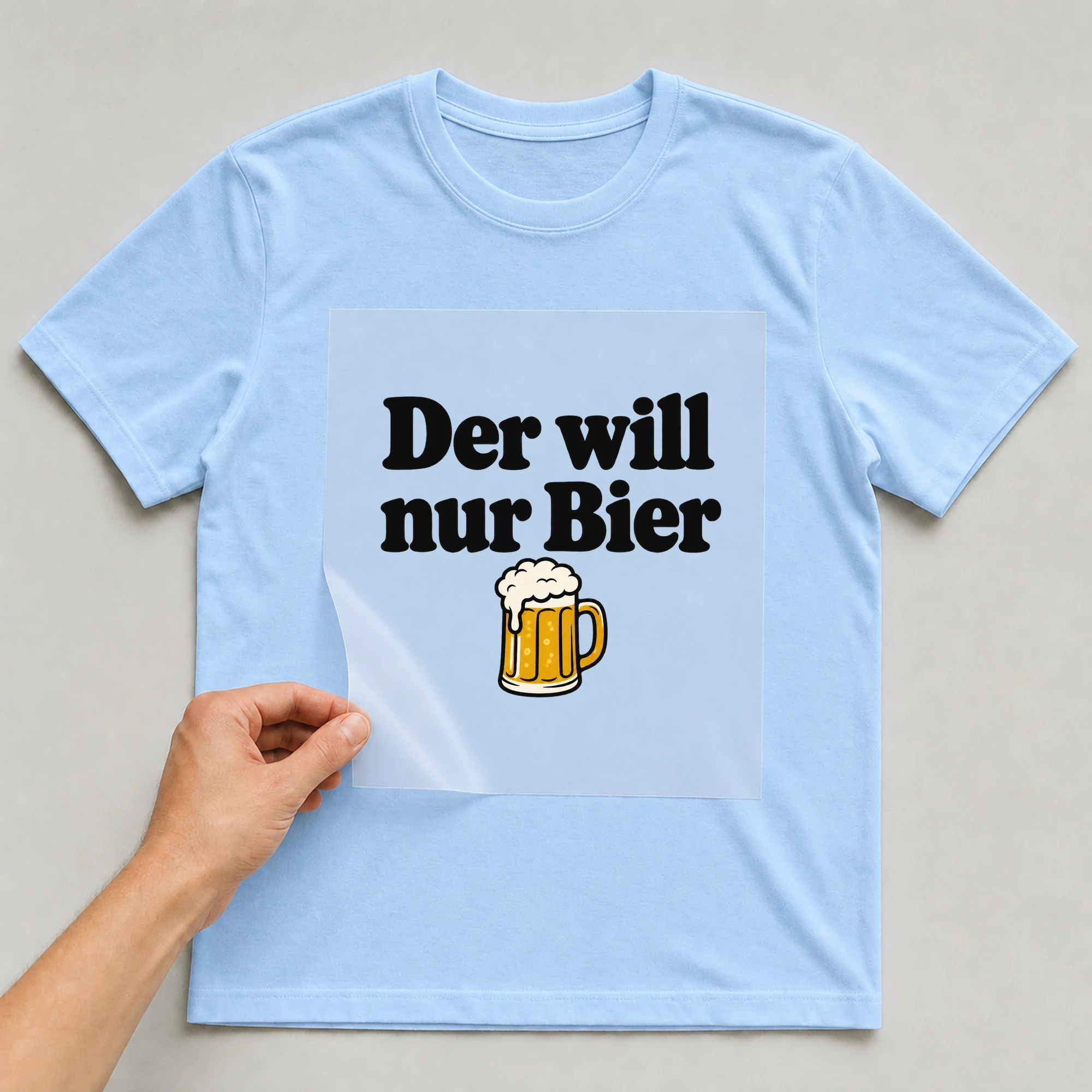 Bügelbild „Der will nur Bier“ auf babyblauem T-Shirt, Folie wird aufgelegt