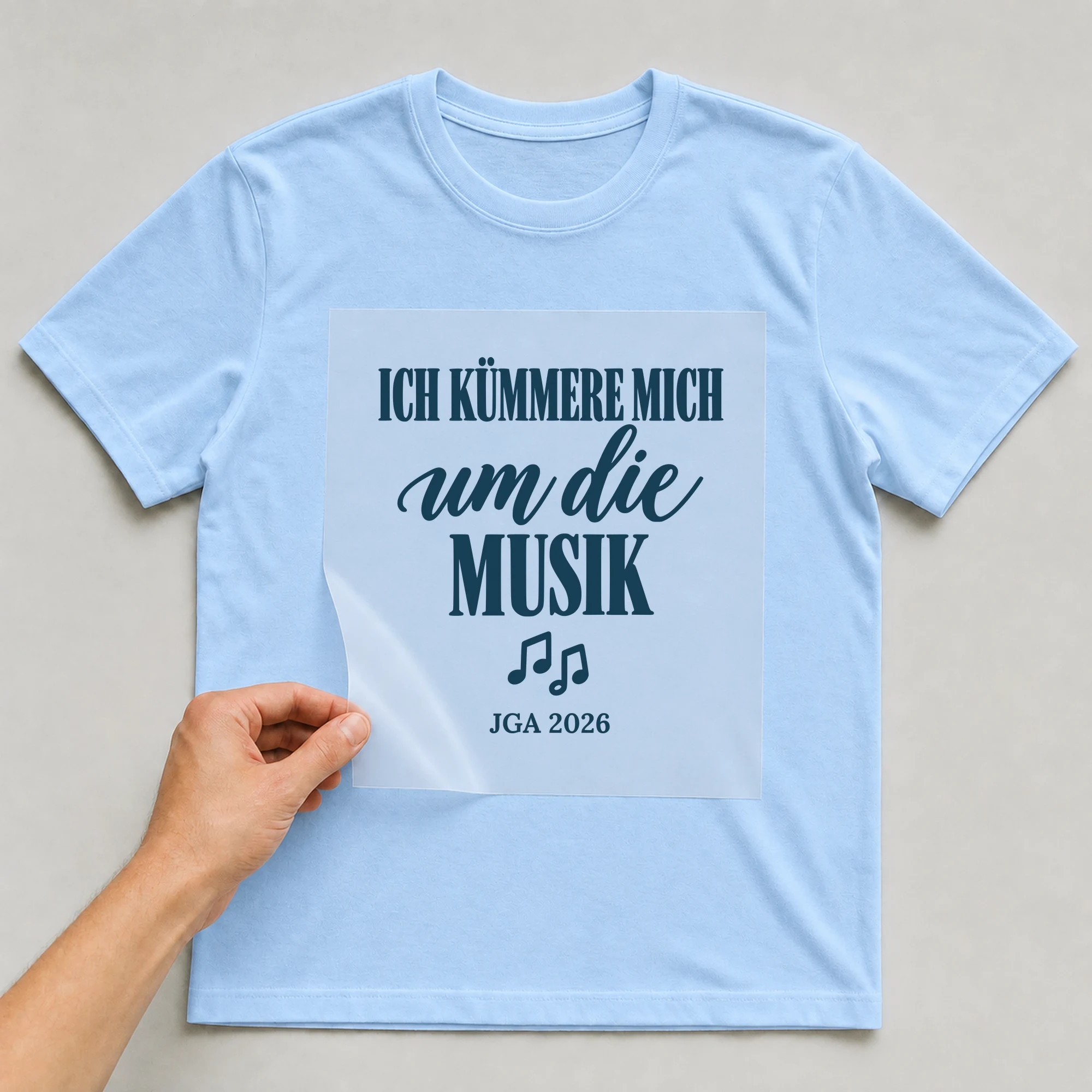 Bügelbild Ich kümmere mich um die Musik mit Jahr auf hellblauem T-Shirt, Folie wird aufgelegt