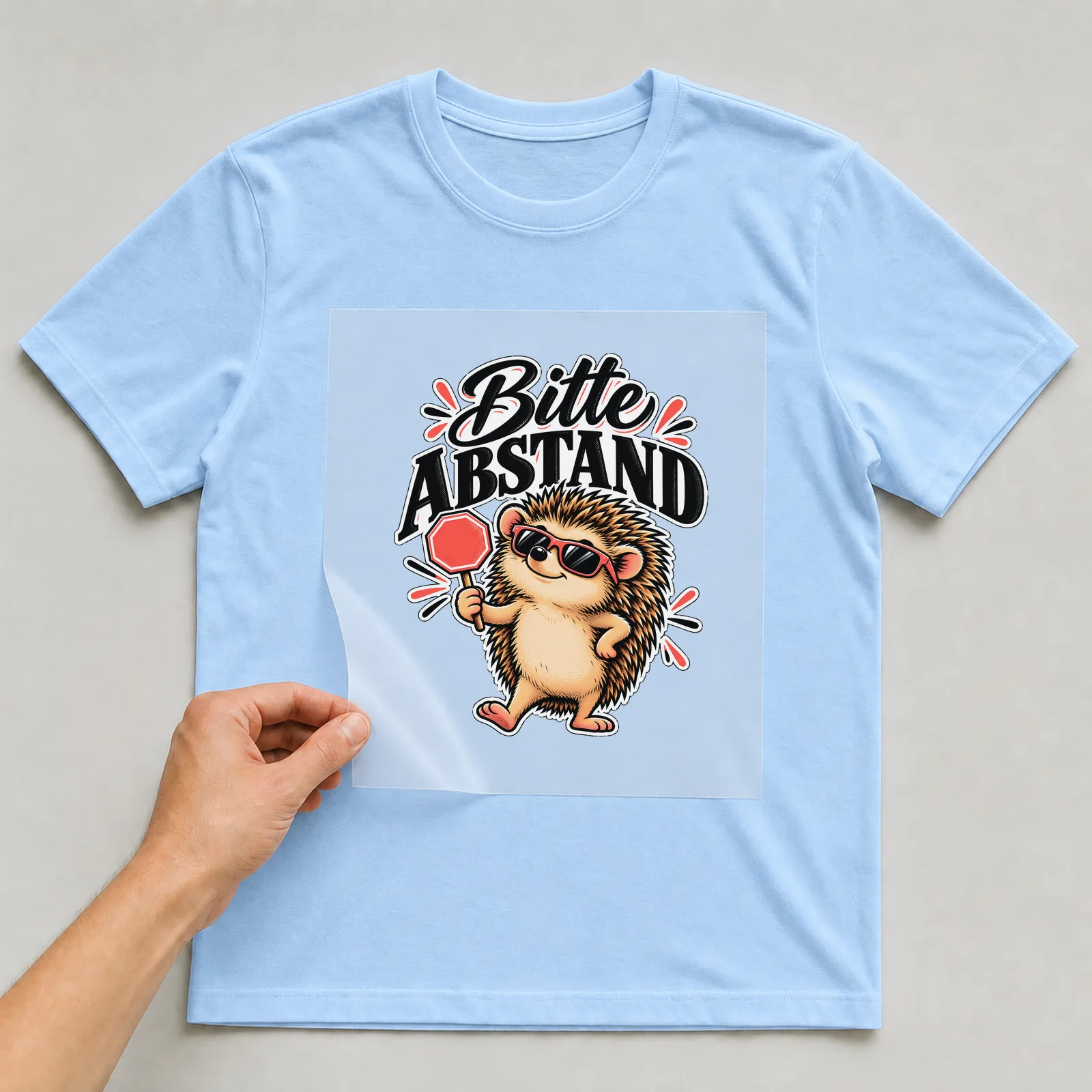 Bügelbild „Bitte Abstand“ auf hellblauem T-Shirt, Folie wird aufgelegt
