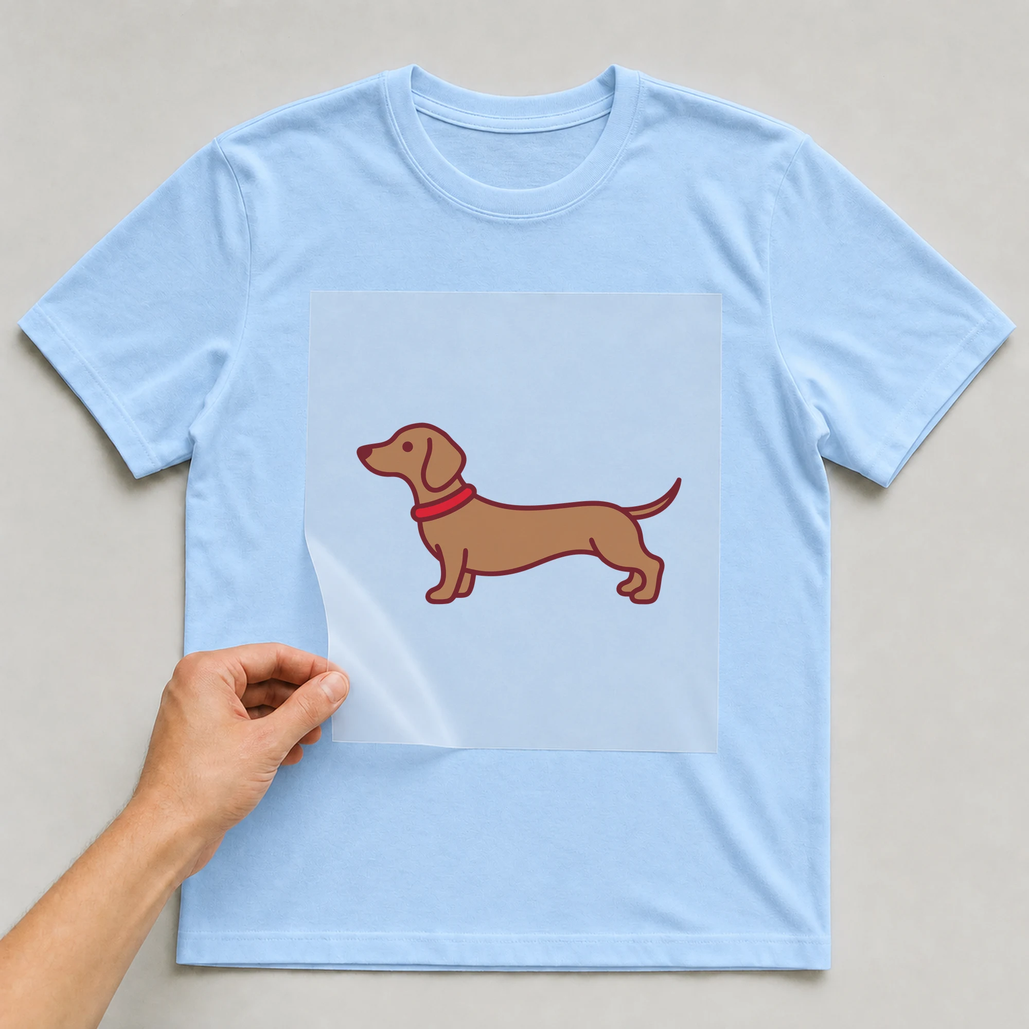 Bügelbild „Dackel“ auf babyblauem T-Shirt, Folie wird aufgelegt