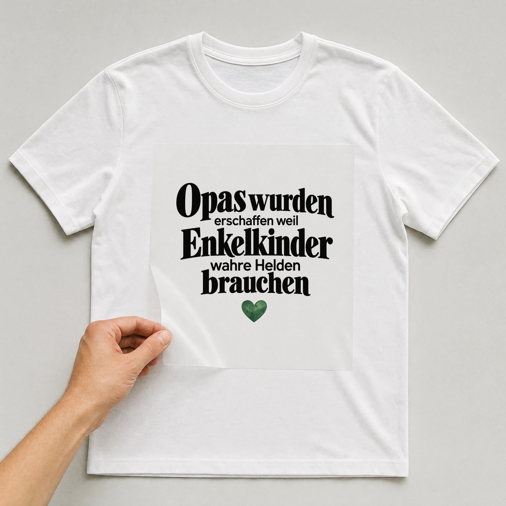 Bügelbild „Opas wurden erschaffen weil Enkelkinder wahre Helden brauchen“ auf weißem T-Shirt, Folie wird aufgelegt