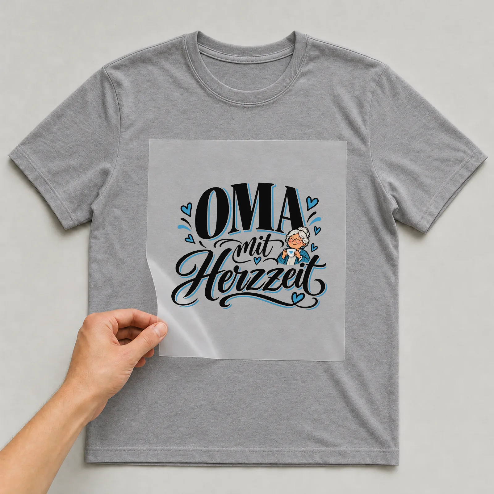 Bügelbild „Oma mit Herzzeit“ auf grauem T-Shirt, Folie wird aufgelegt