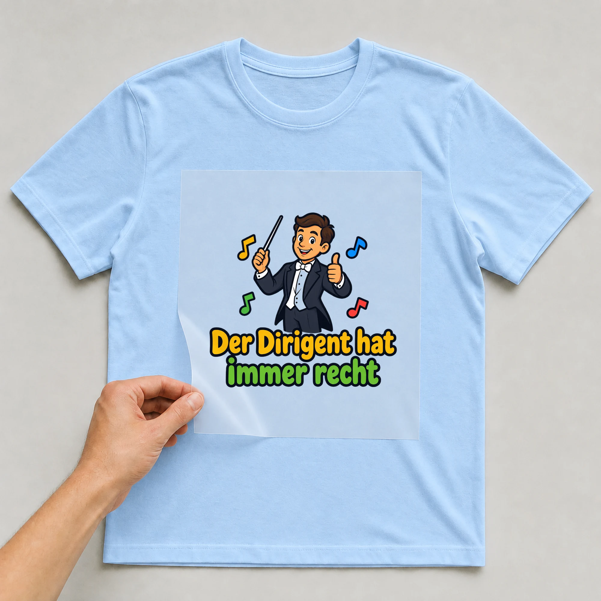 Bügelbild „Der Dirigent hat immer recht“ auf babyblauem T-Shirt, Folie wird aufgelegt