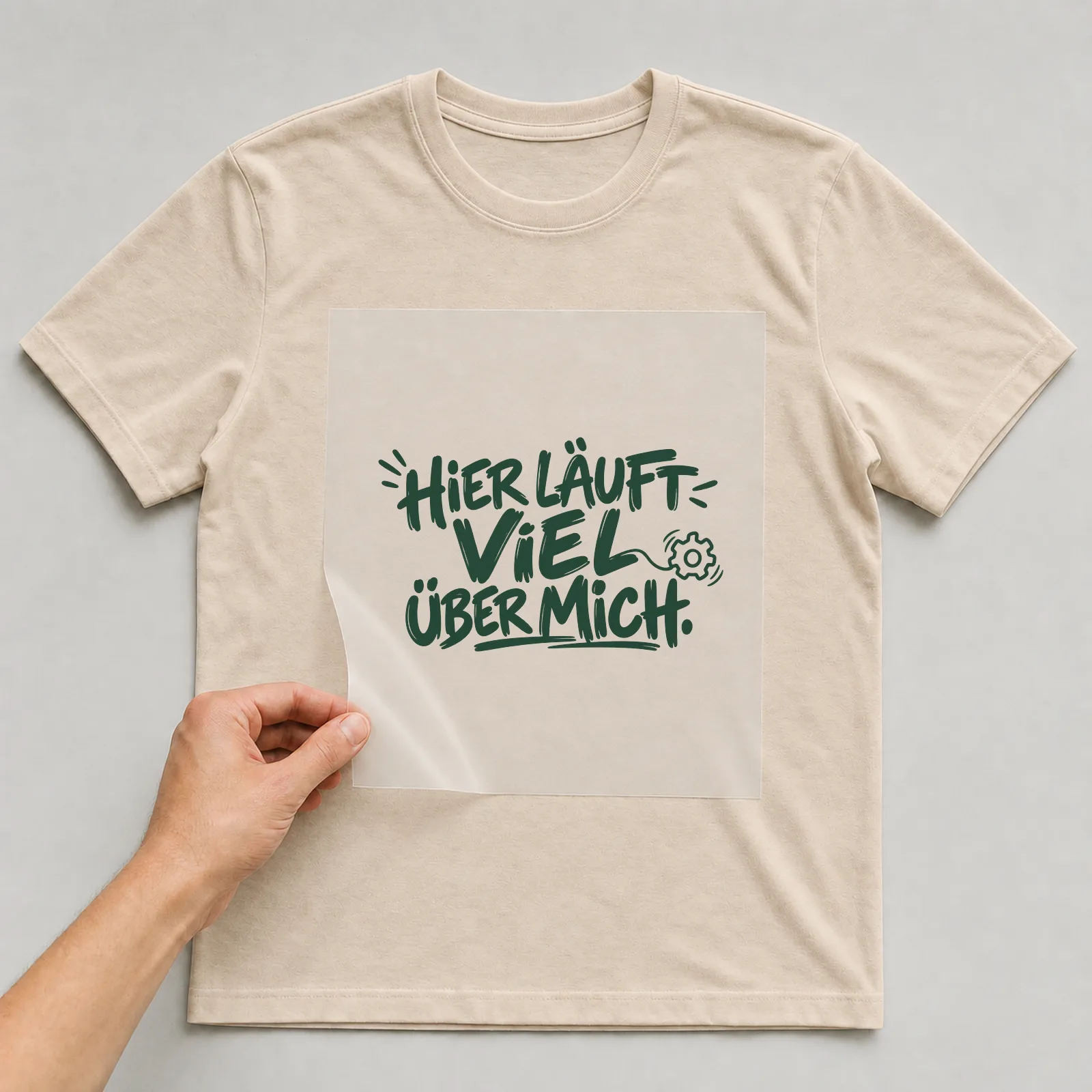 Bügelbild „Hier läuft viel über mich“ auf beigem T-Shirt, Folie wird aufgelegt