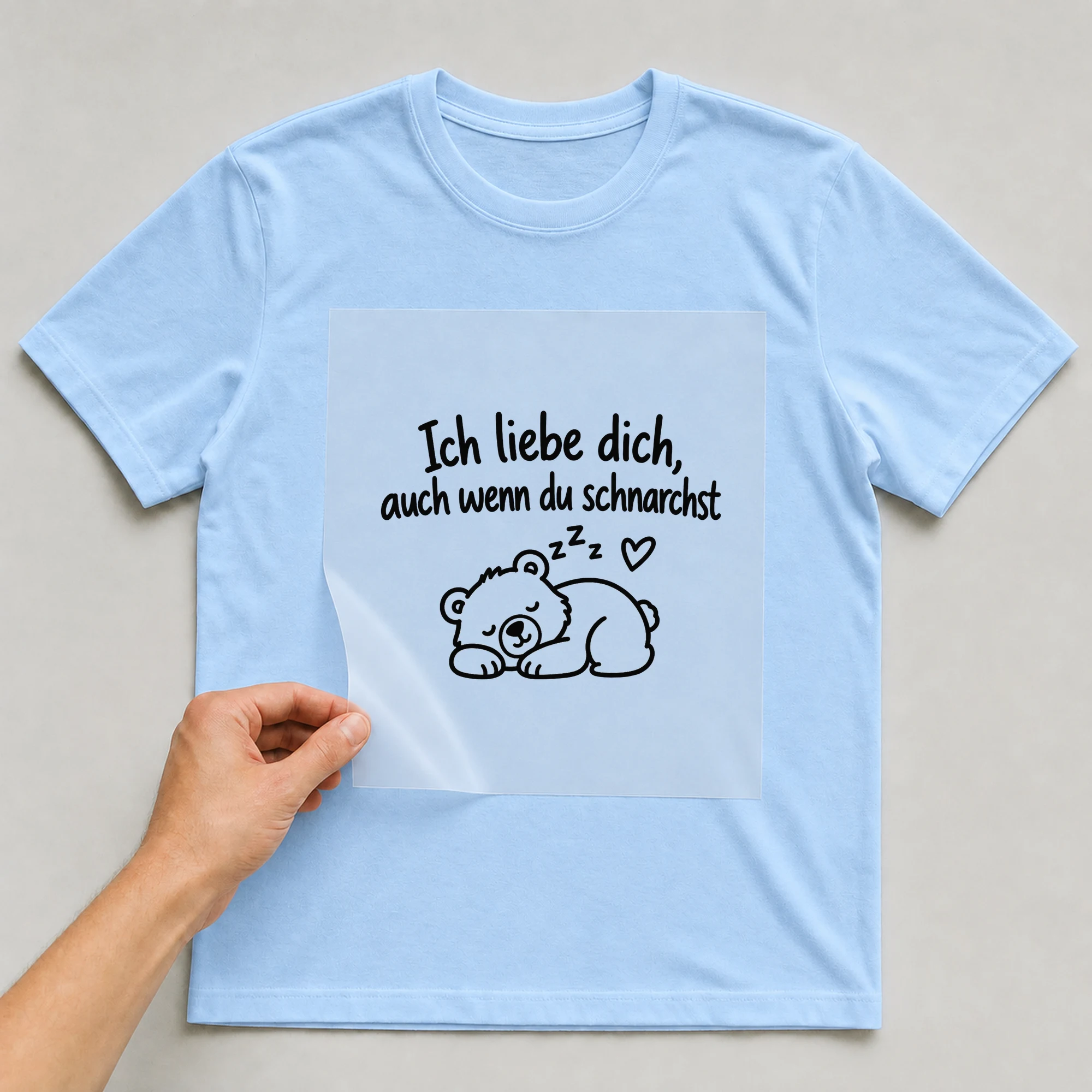 Bügelbild „Ich liebe dich, auch wenn du schnarchst“ auf babyblauem T-Shirt, Folie wird aufgelegt