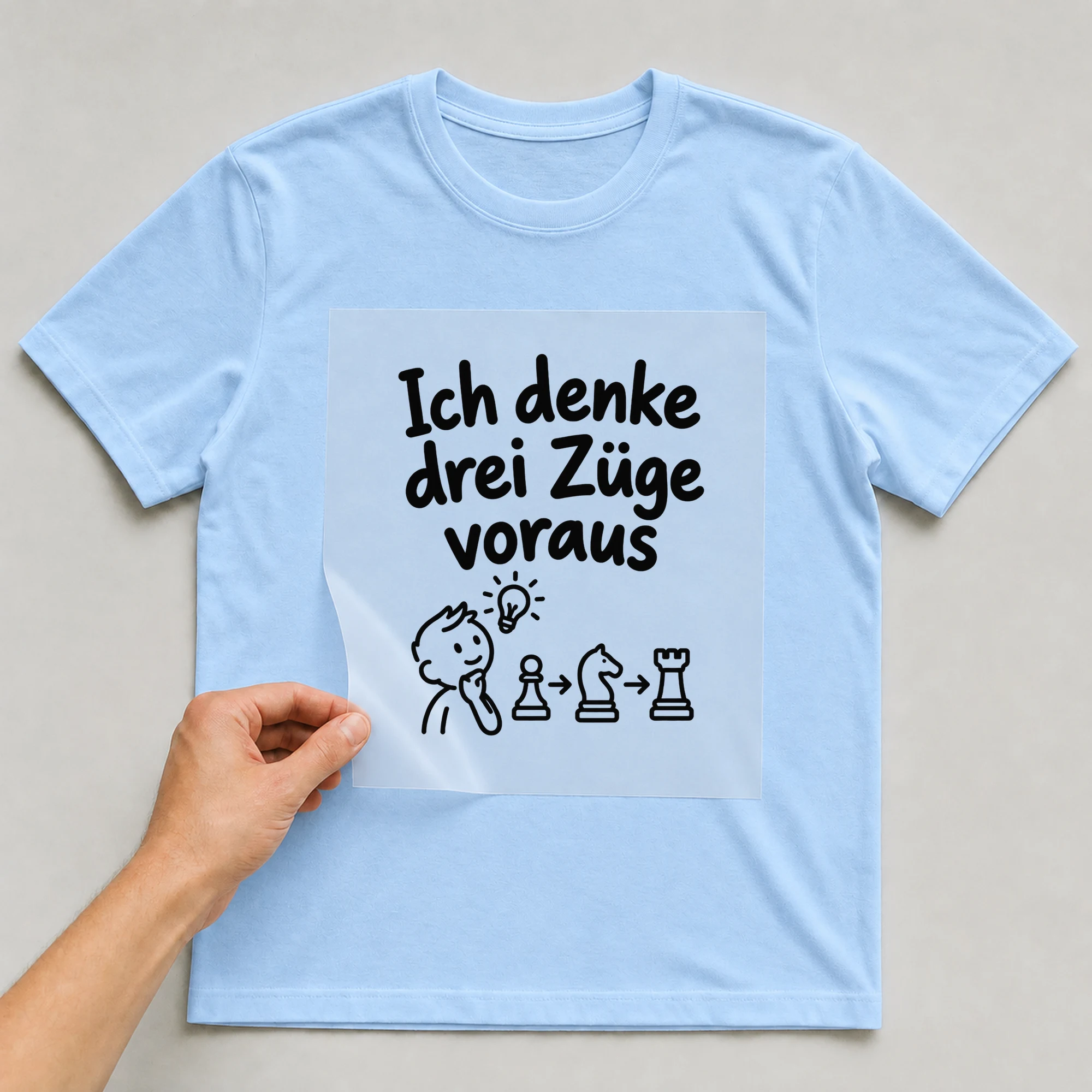 Bügelbild „Ich denke drei Züge voraus“ auf babyblauem T-Shirt, Folie wird aufgelegt