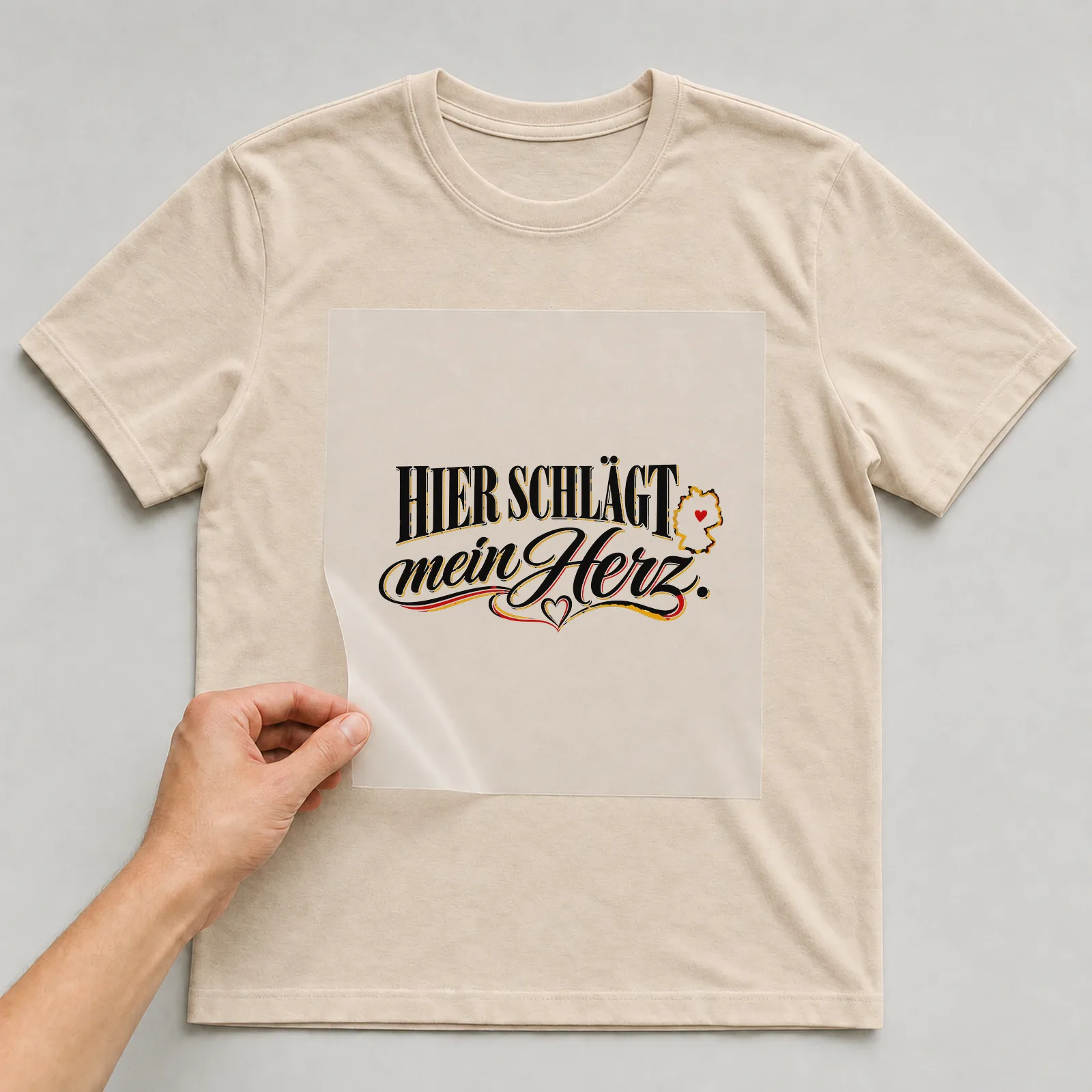 Bügelbild „Hier schlägt mein Herz“ auf beigem T-Shirt, Folie wird aufgelegt