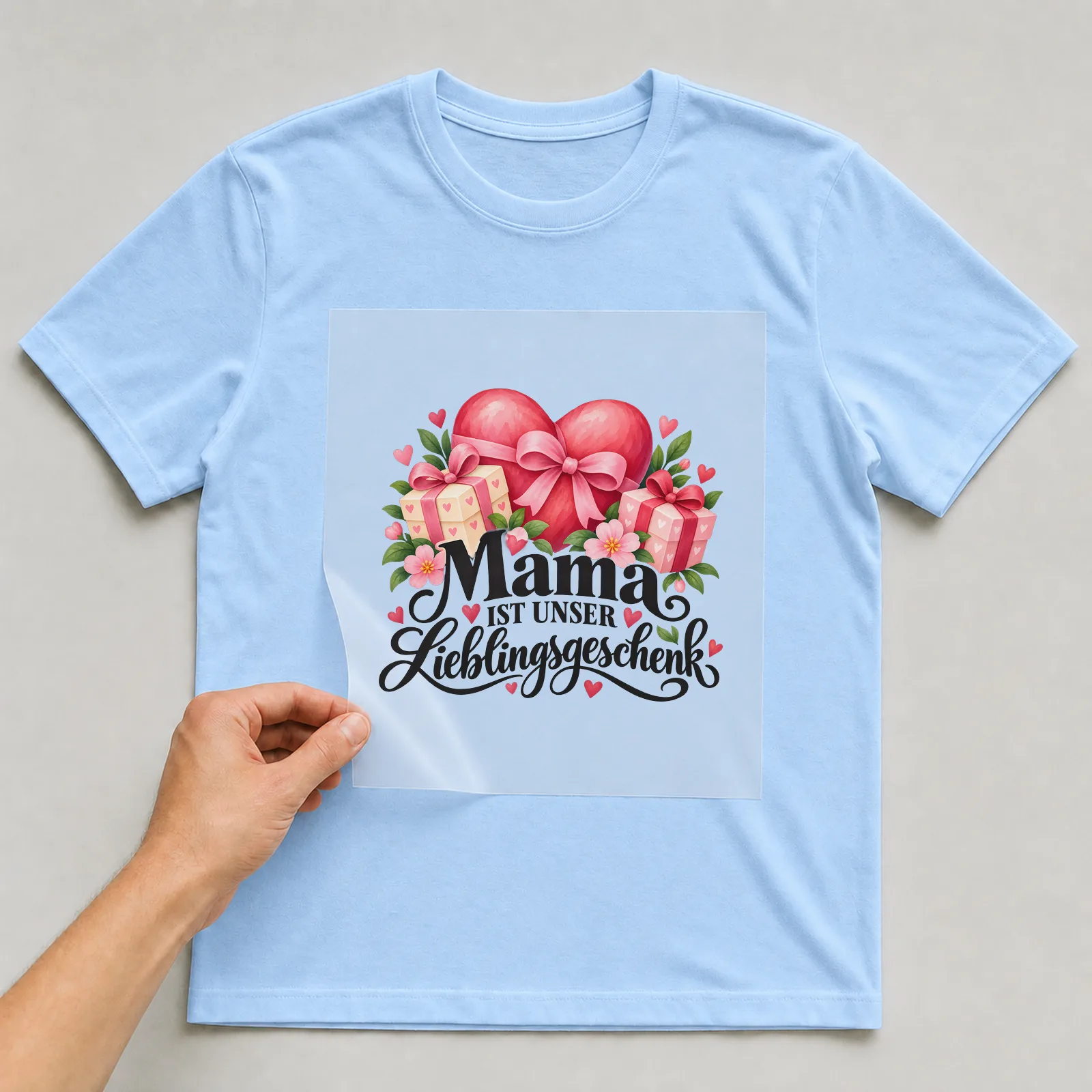 Bügelbild „Mama ist unser Lieblingsgeschenk“ auf hellblauem T-Shirt, Folie wird aufgelegt