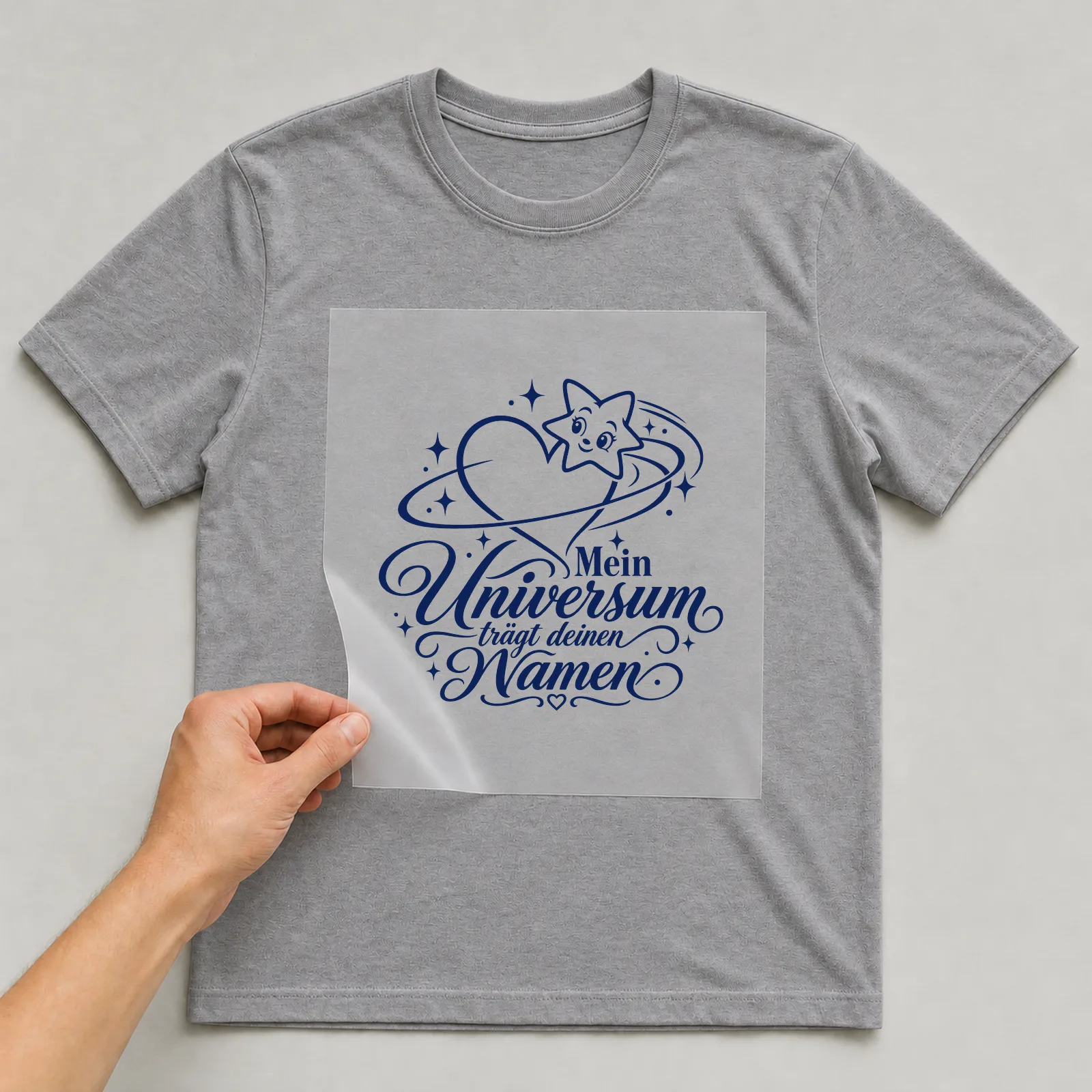 Bügelbild „Mein Universum trägt deinen Namen“ auf grauem T-Shirt, Folie wird aufgelegt