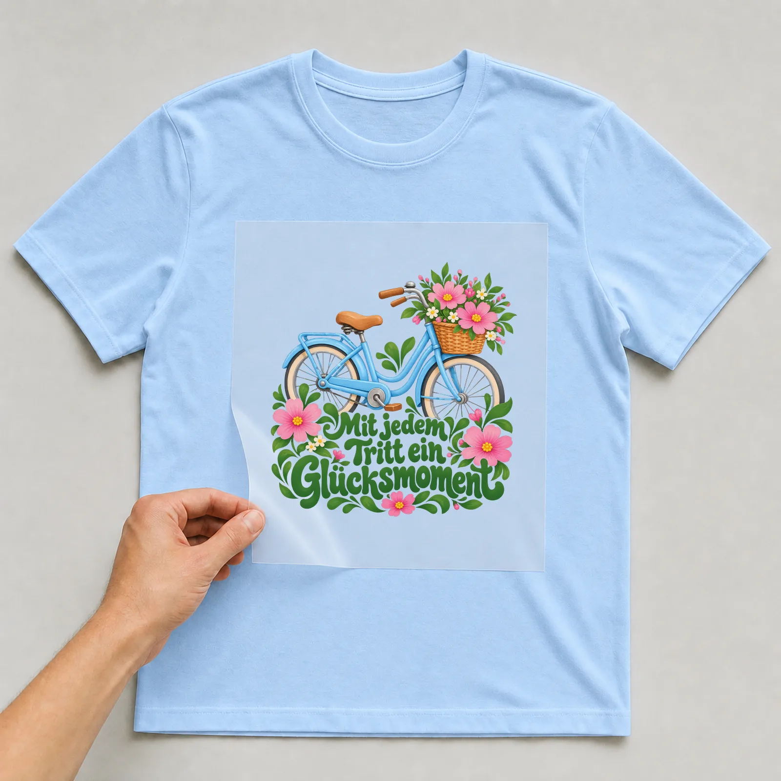 Bügelbild „Mit jedem Tritt ein Glücksmoment“ auf hellblauem T-Shirt, Folie wird aufgelegt