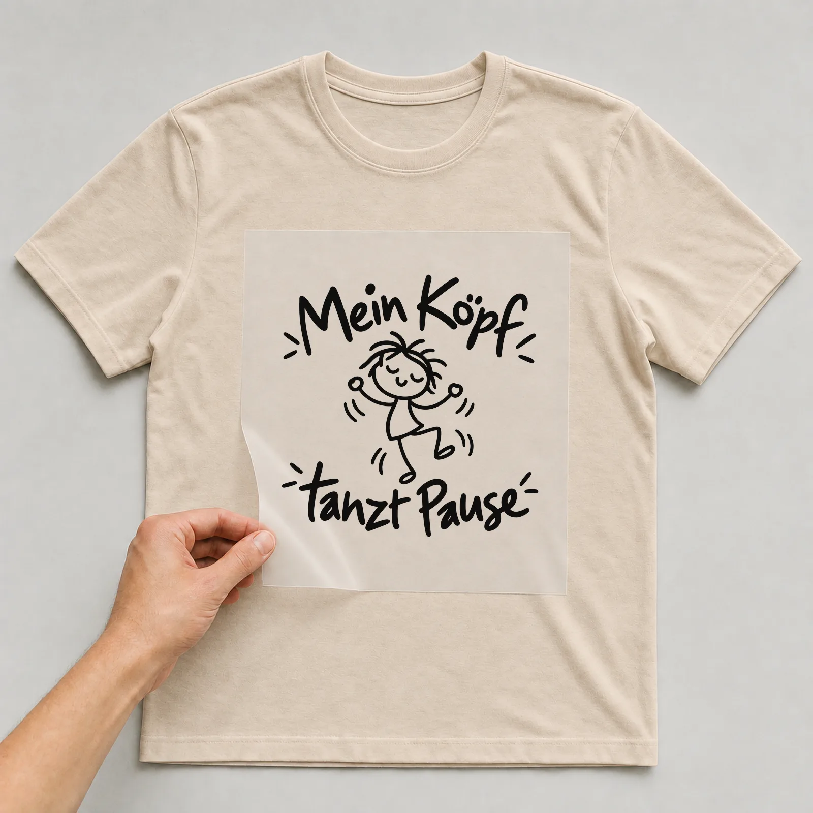 Bügelbild „Mein Kopf tanzt Pause“ auf beigem T-Shirt, Folie wird aufgelegt