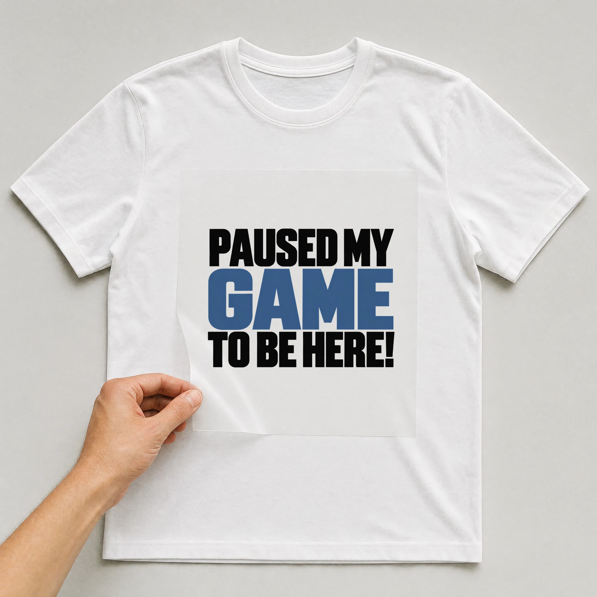 Bügelbild „Paused My Game To Be Here!“ auf weißem T-Shirt, Folie wird aufgelegt