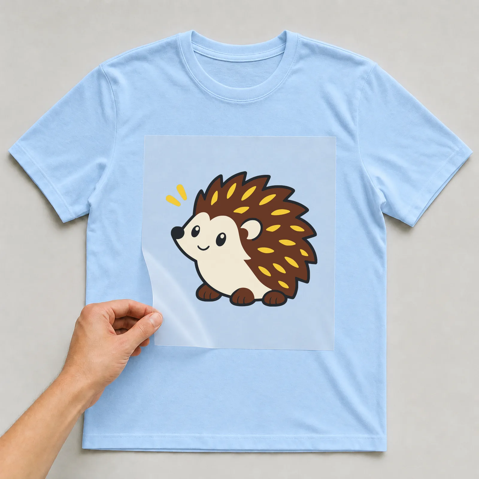 Bügelbild Igel im Comic-Stil auf hellblauem T-Shirt, Folie wird aufgelegt