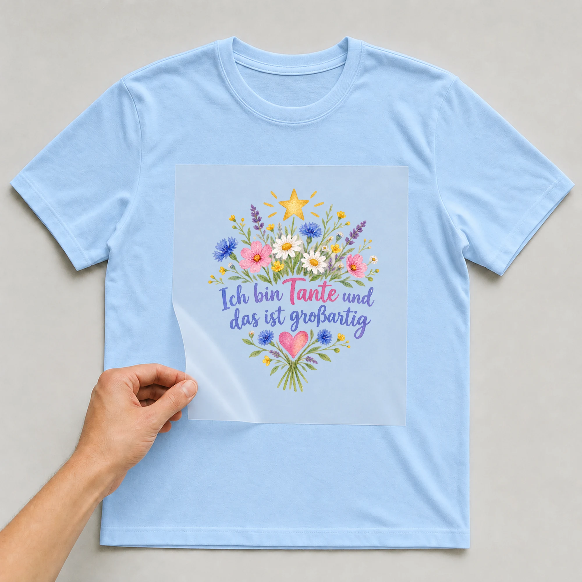 Bügelbild „Ich bin Tante und das ist großartig“ auf babyblauem T-Shirt, Folie wird aufgelegt