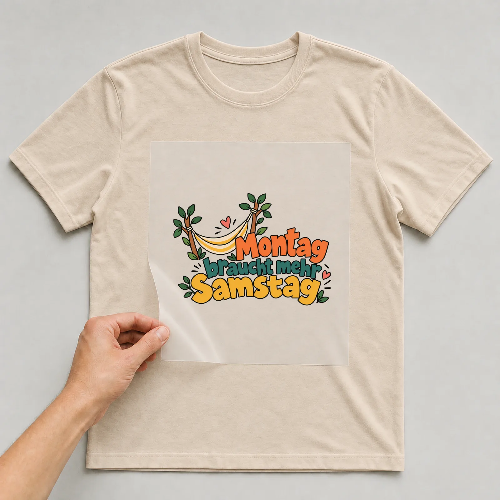 Bügelbild „Montag braucht mehr Samstag“ auf beigem T-Shirt, Folie wird aufgelegt