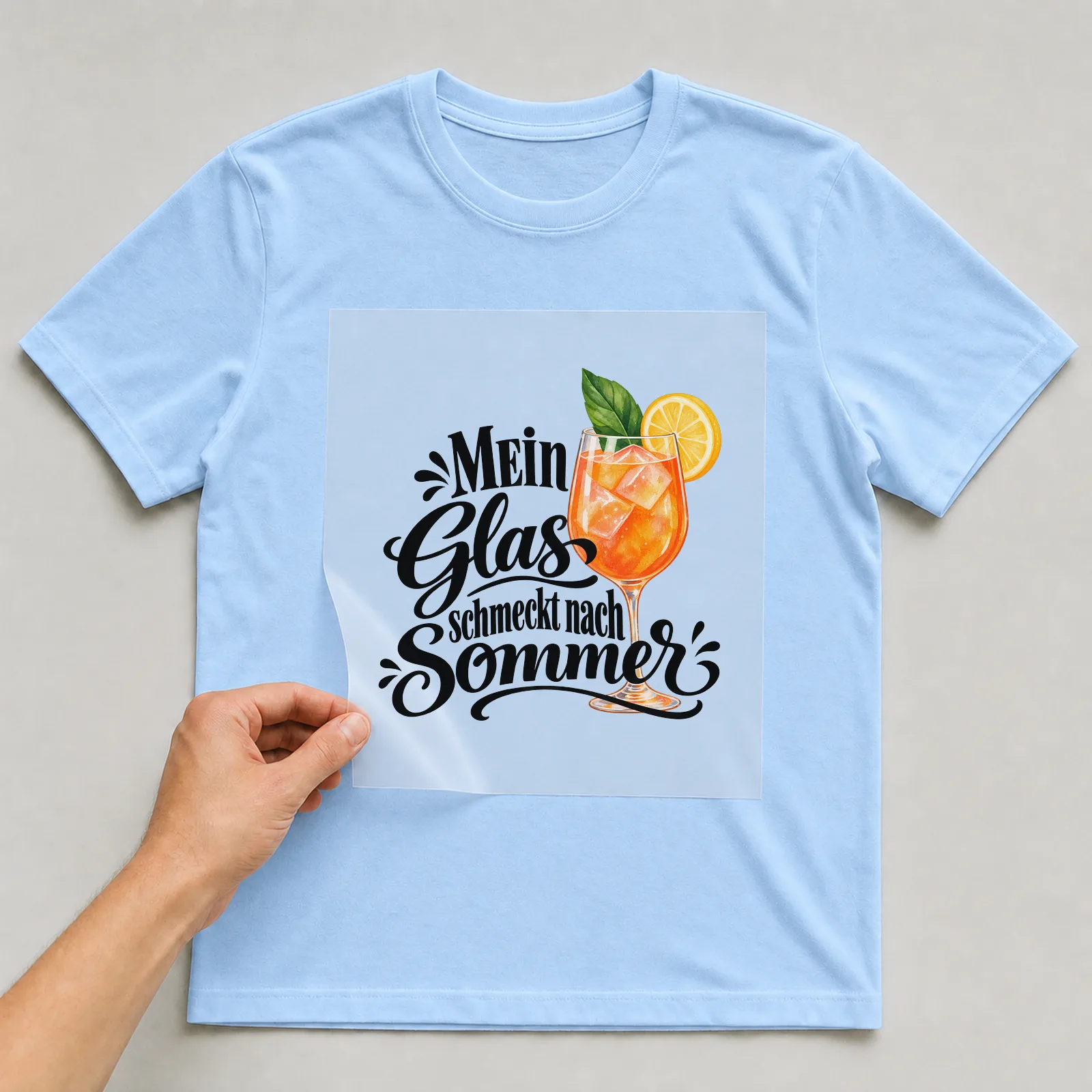 Bügelbild „Mein Glas schmeckt nach Sommer“ auf hellblauem T-Shirt, Folie wird aufgelegt