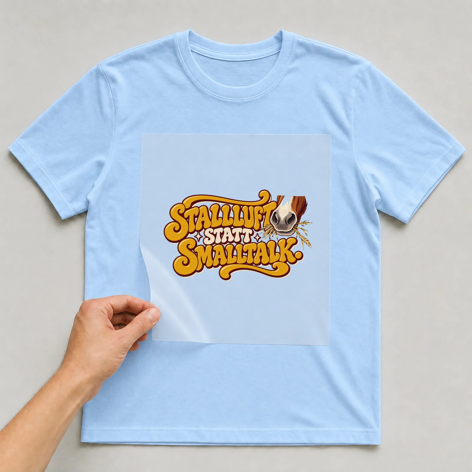 Bügelbild „Stallluft statt Smalltalk“ auf hellblauem T-Shirt, Folie wird aufgelegt