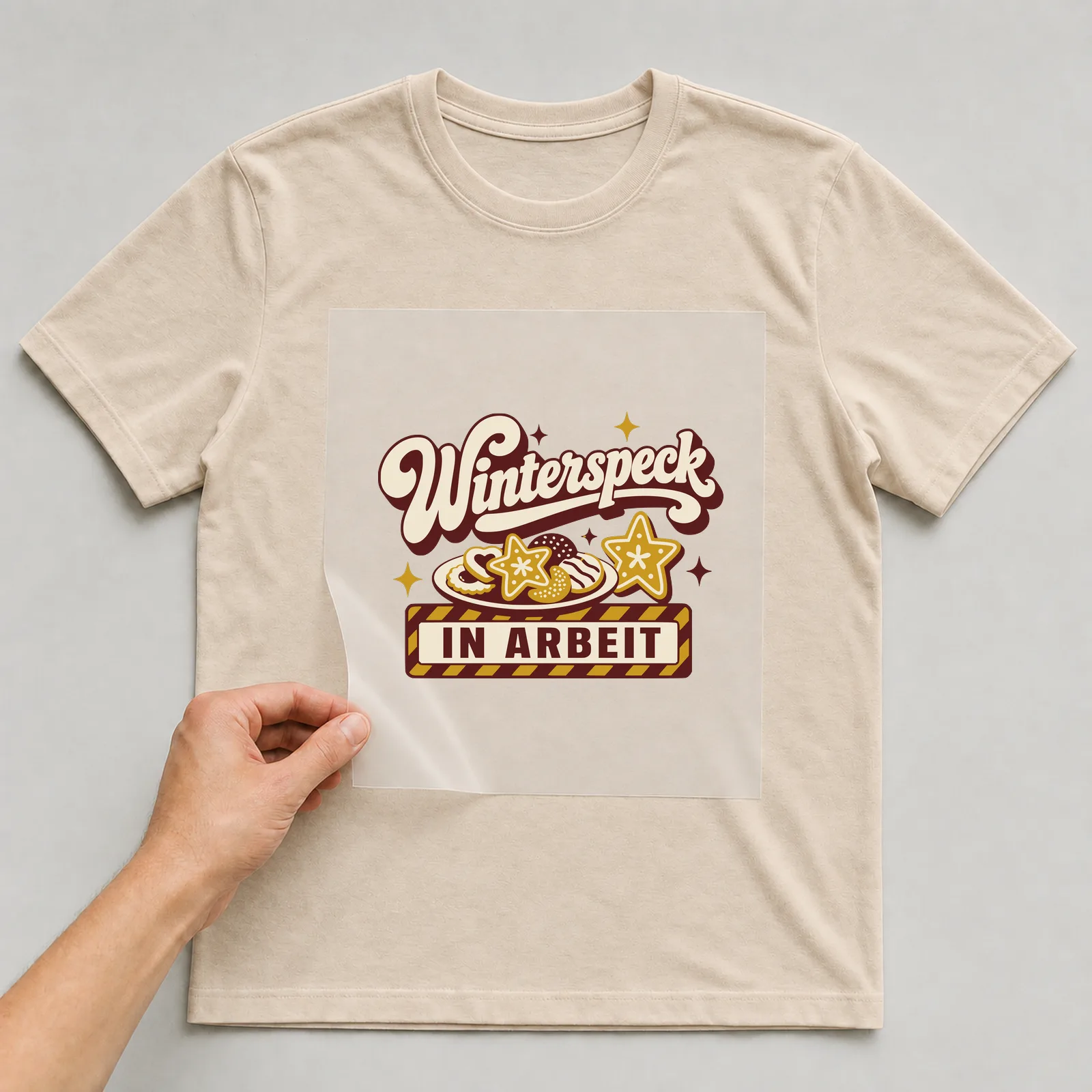 Bügelbild Winterspeck in Arbeit auf beigem T-Shirt, Folie wird aufgelegt
