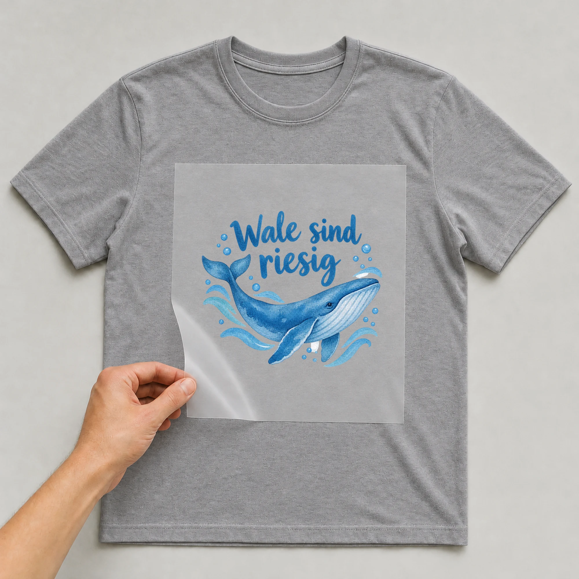 Bügelbild „Wale sind riesig“ auf grauem T-Shirt, Folie wird aufgelegt