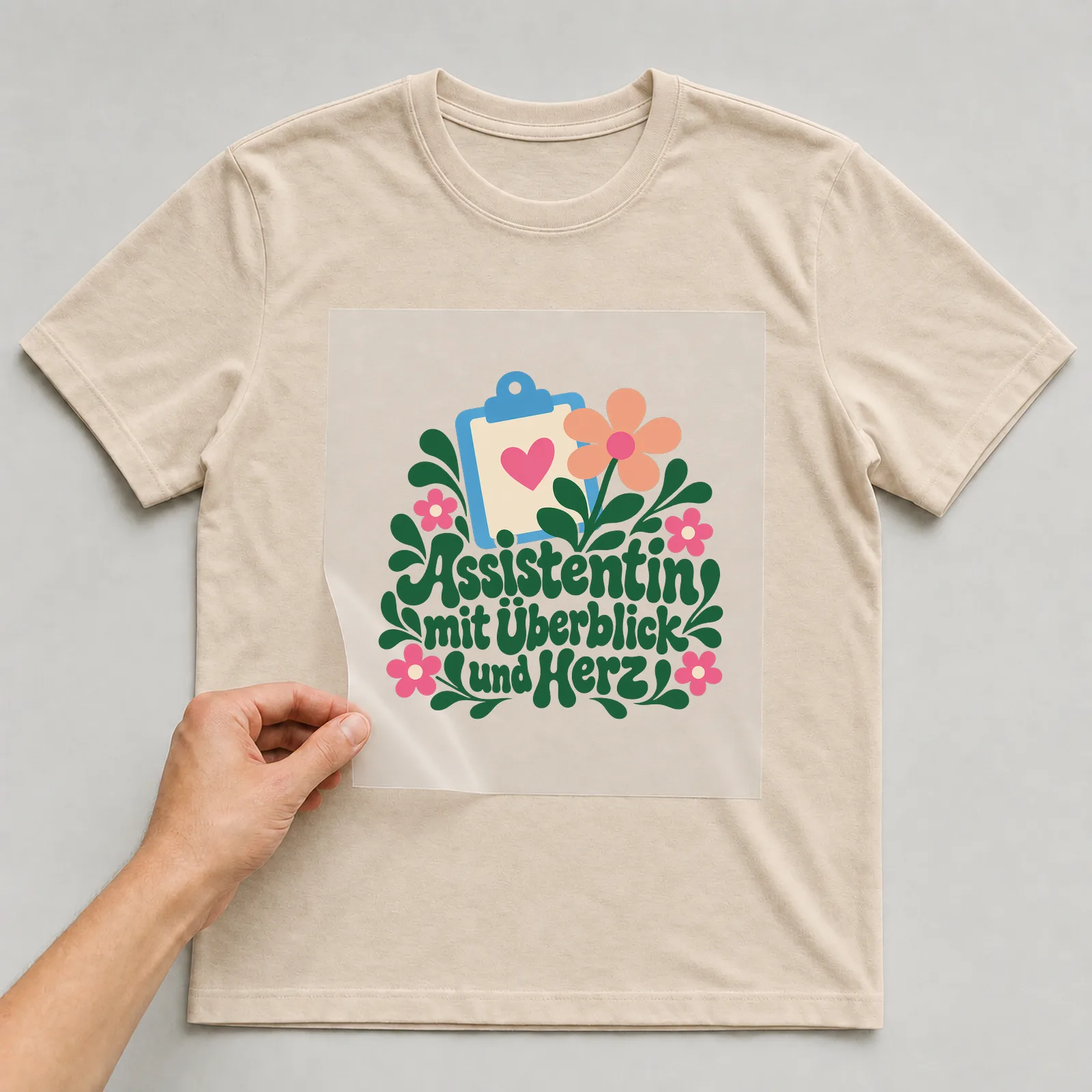 Bügelbild „Assistentin mit Überblick und Herz“ auf beigem T-Shirt, Folie wird aufgelegt