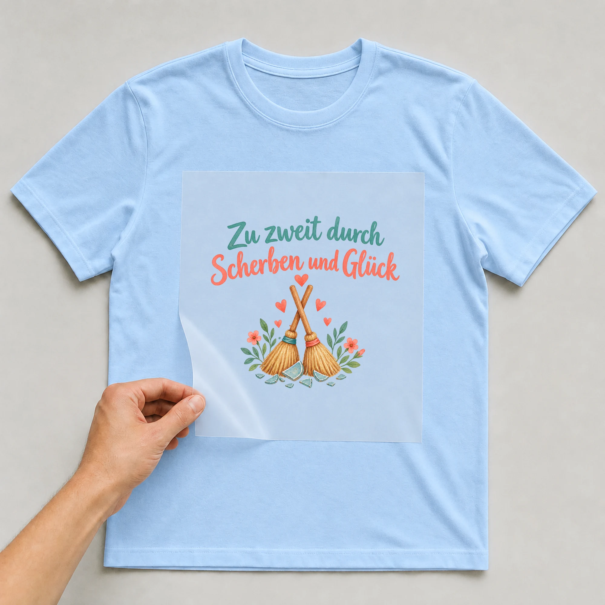 Bügelbild „Zu zweit durch Scherben und Glück“ auf babyblauem T-Shirt, Folie wird aufgelegt