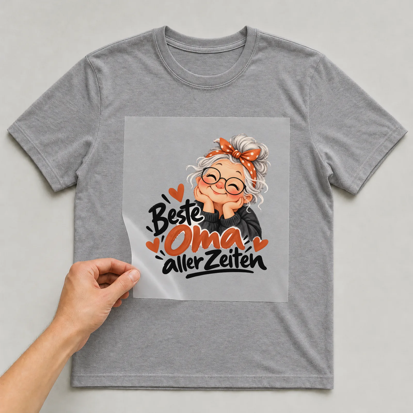 Bügelbild „Beste Oma aller Zeiten“ auf grauem T-Shirt, Folie wird aufgelegt