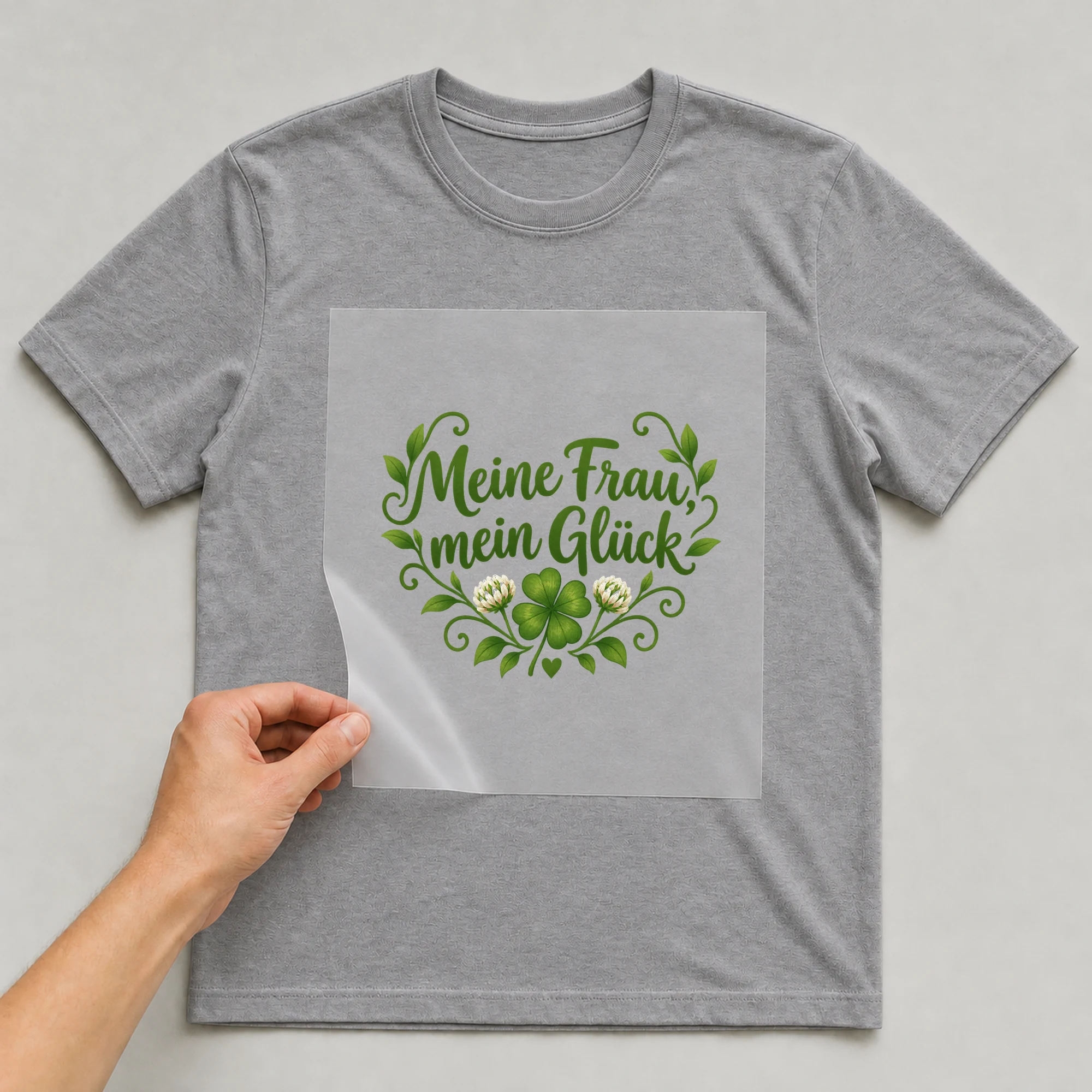 Bügelbild „Meine Frau, mein Glück“ auf grauem T-Shirt, Folie wird aufgelegt