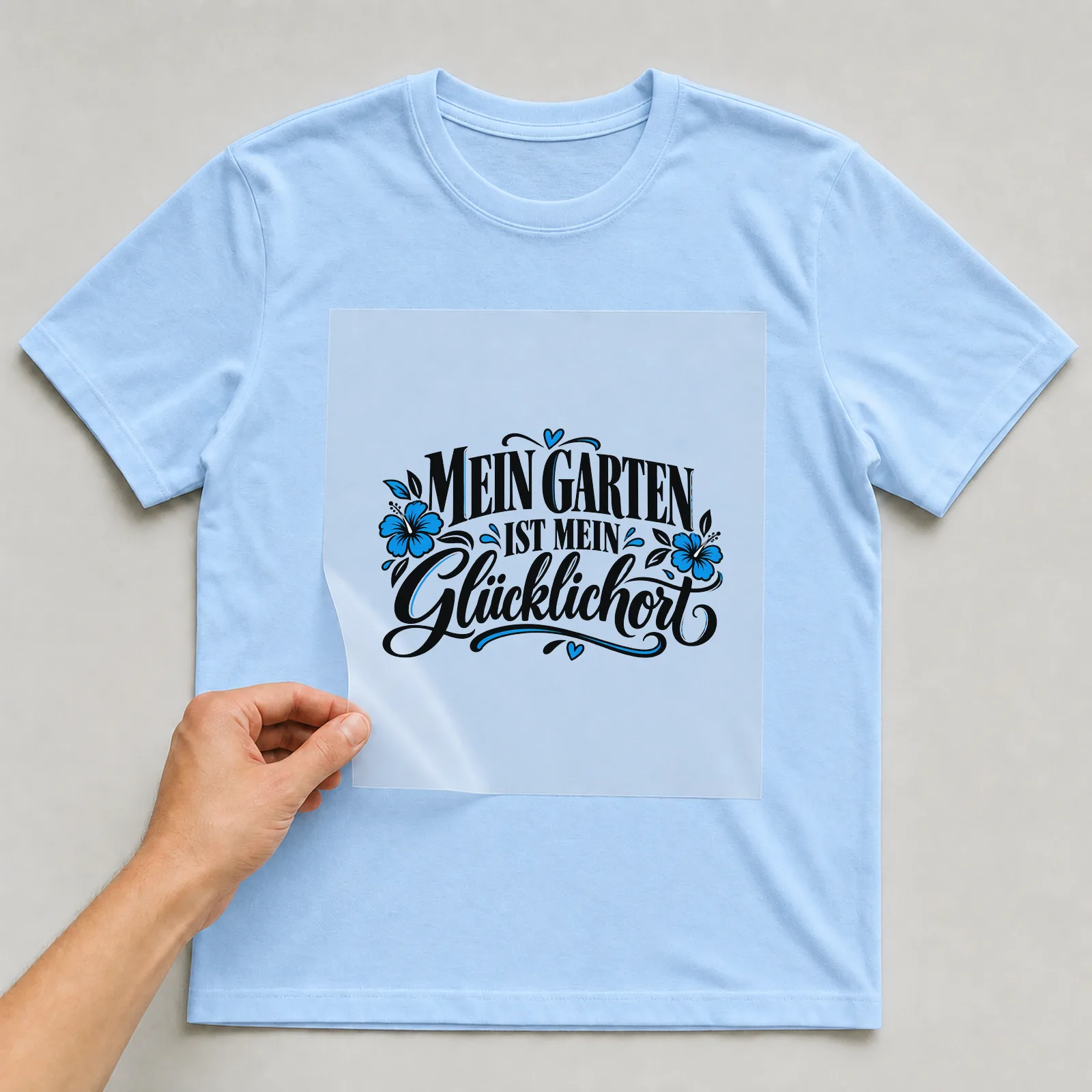 Bügelbild „Mein Garten ist mein Glücklichort“ auf hellblauem T-Shirt, Folie wird aufgelegt