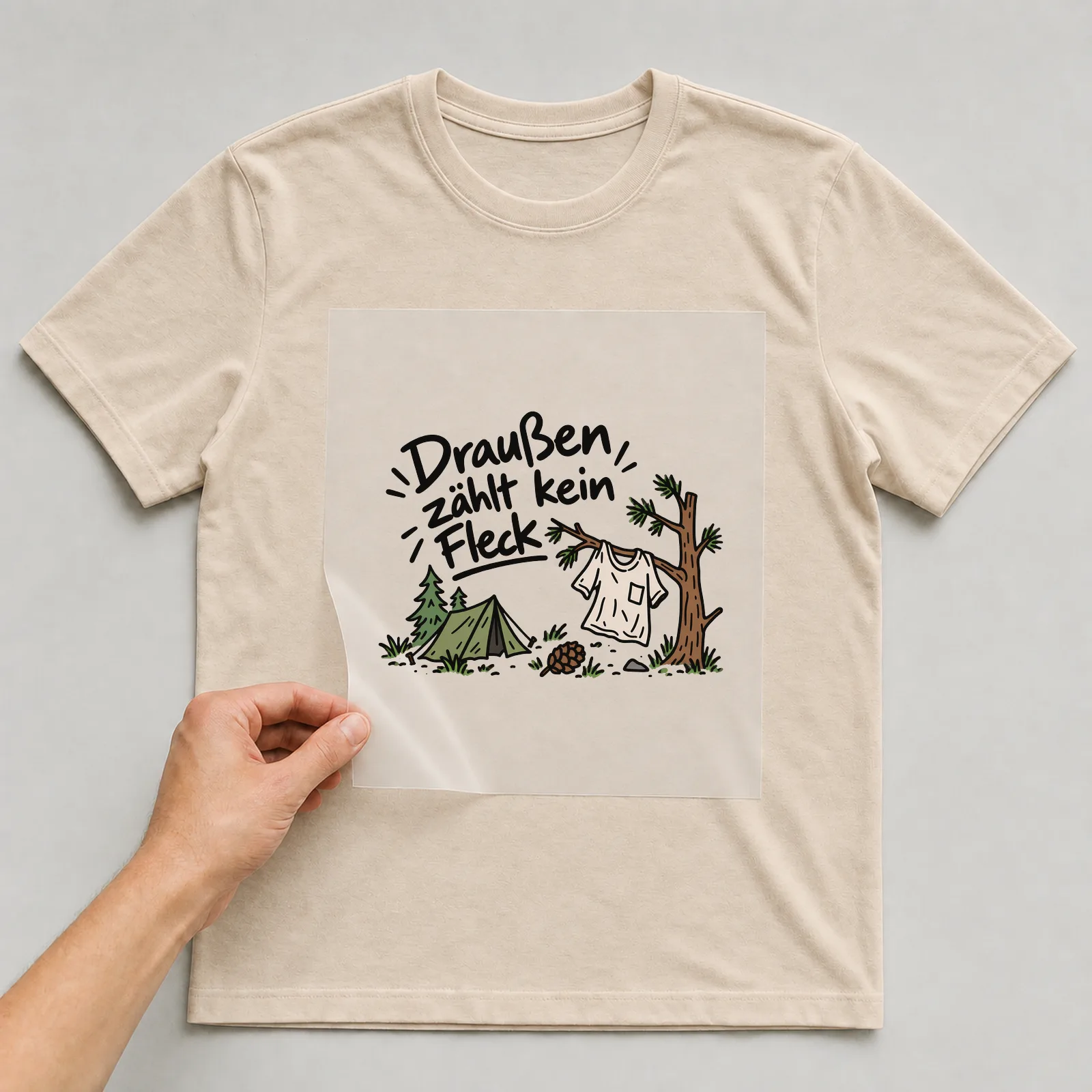 Bügelbild „Draußen zählt kein Fleck“ auf beigem T-Shirt, Folie wird aufgelegt