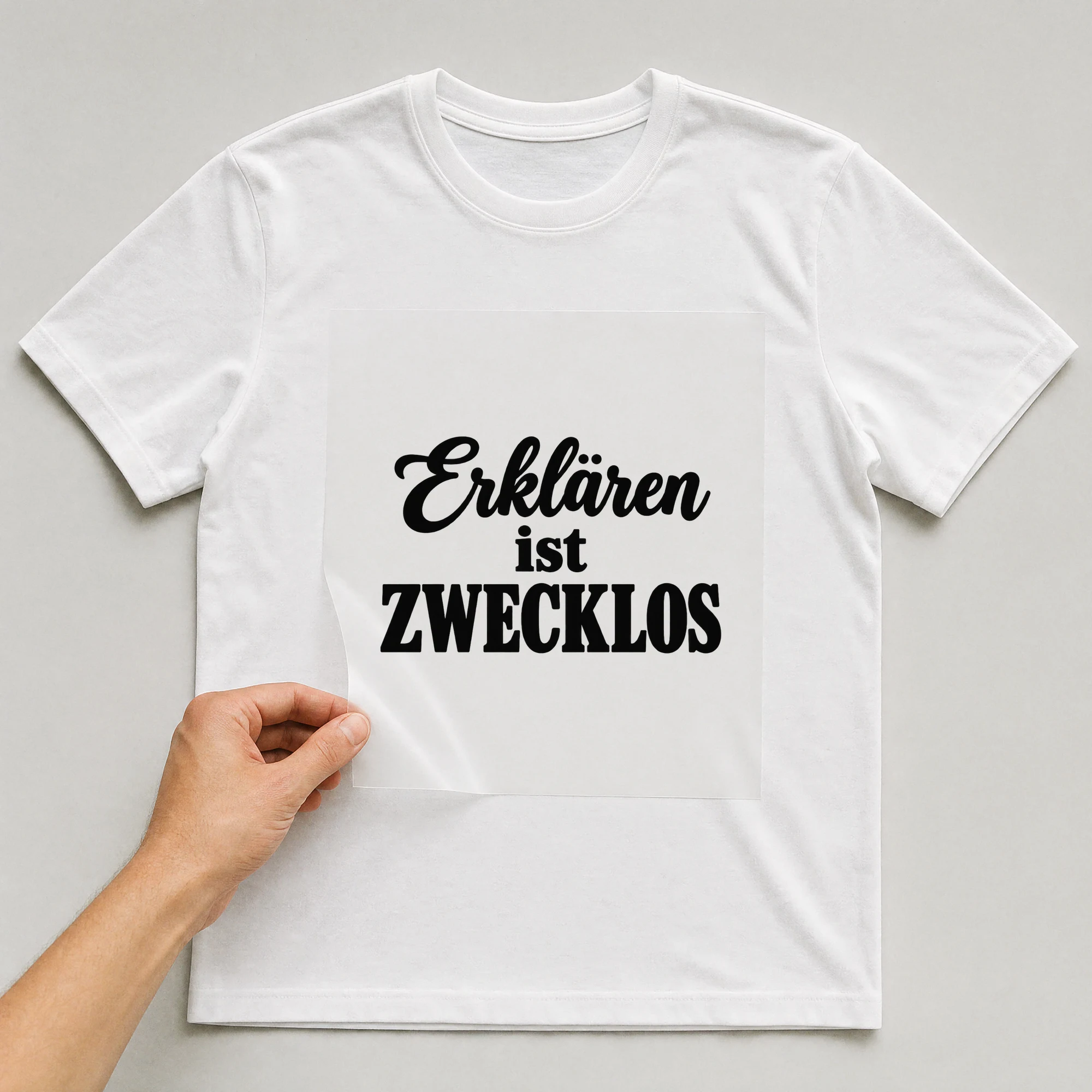Bügelbild „Erklären ist zwecklos“ auf weißem T-Shirt, Folie wird aufgelegt
