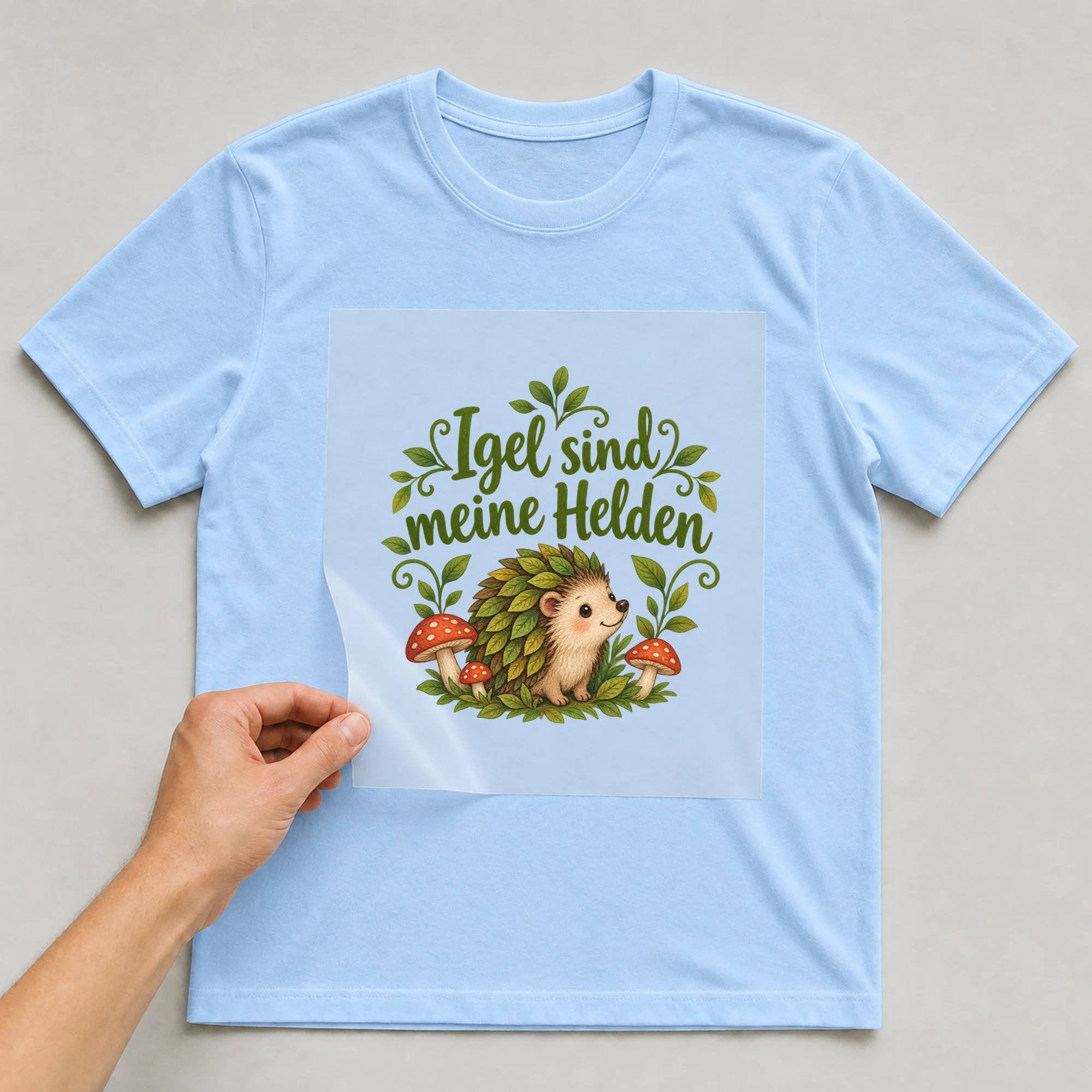 Bügelbild „Igel sind meine Helden“ auf babyblauem T-Shirt, Folie wird aufgelegt