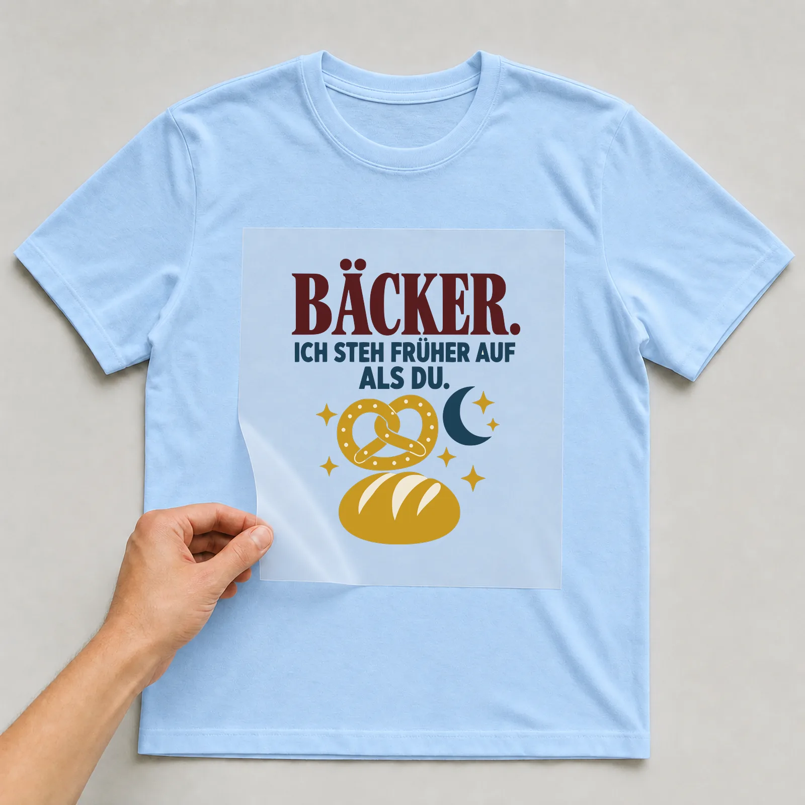 Bügelbild Bäcker. Ich steh früher auf als du. auf hellblauem T-Shirt, Folie wird aufgelegt