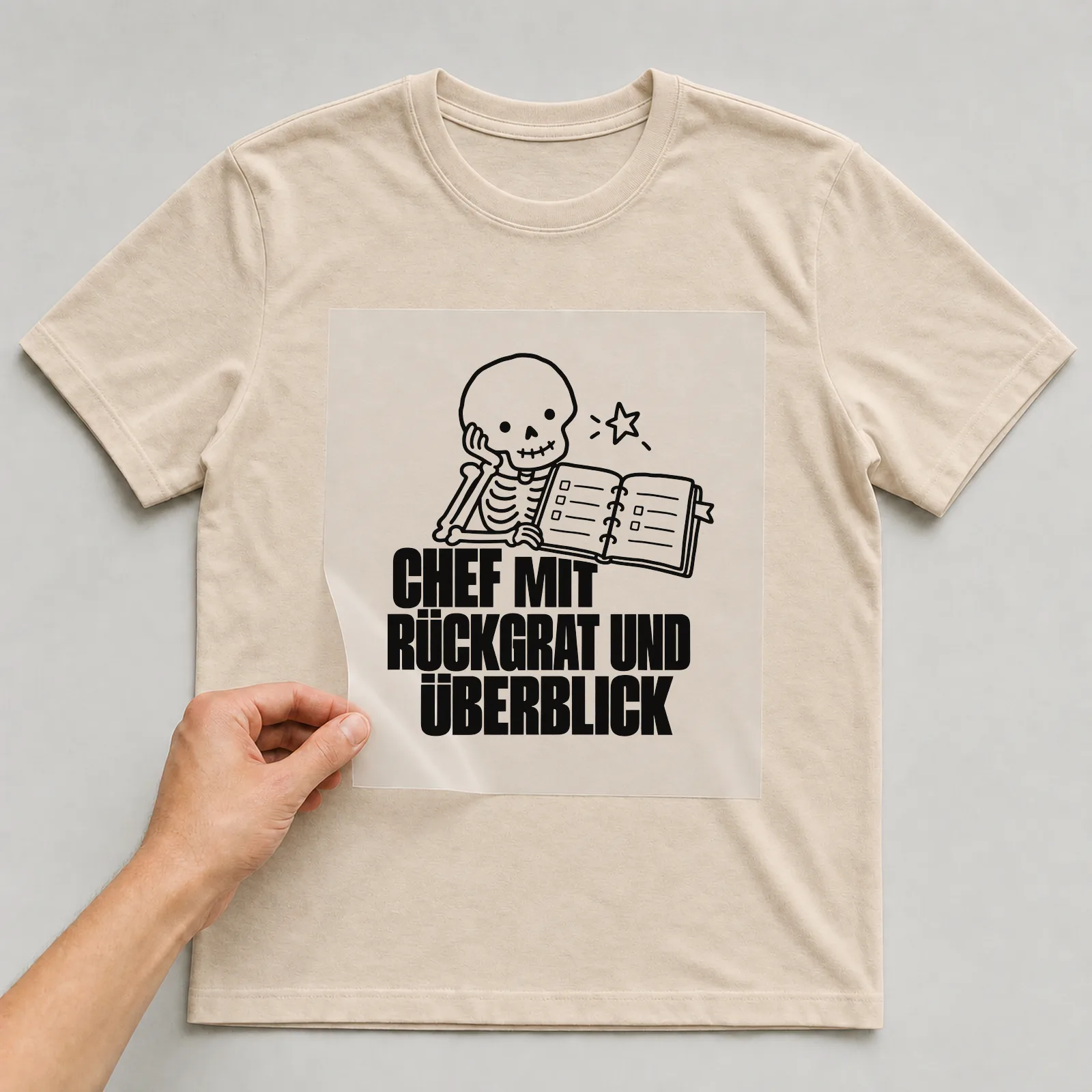 Bügelbild „Chef mit Rückgrat und Überblick“ auf beigem T-Shirt, Folie wird aufgelegt