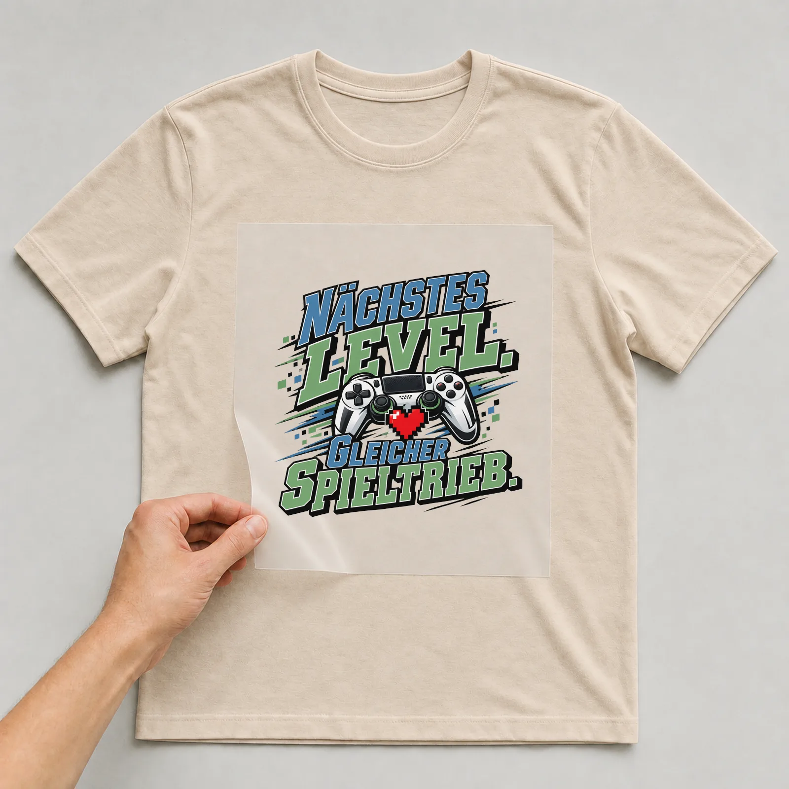 Bügelbild „Nächstes Level. Gleicher Spieltrieb.“ auf beigem T-Shirt, Folie wird aufgelegt