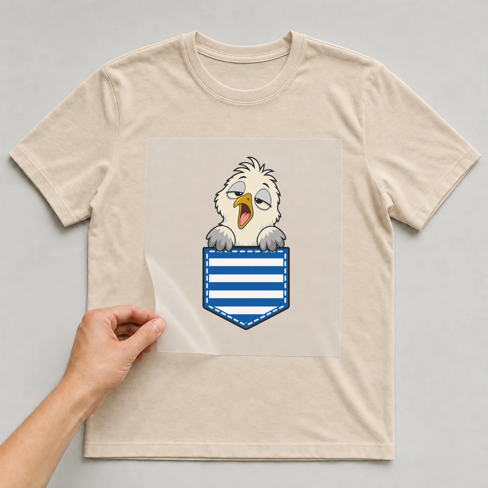 Bügelbild Brusttasche Möwe verschlafen auf beigem T-Shirt, Folie wird aufgelegt