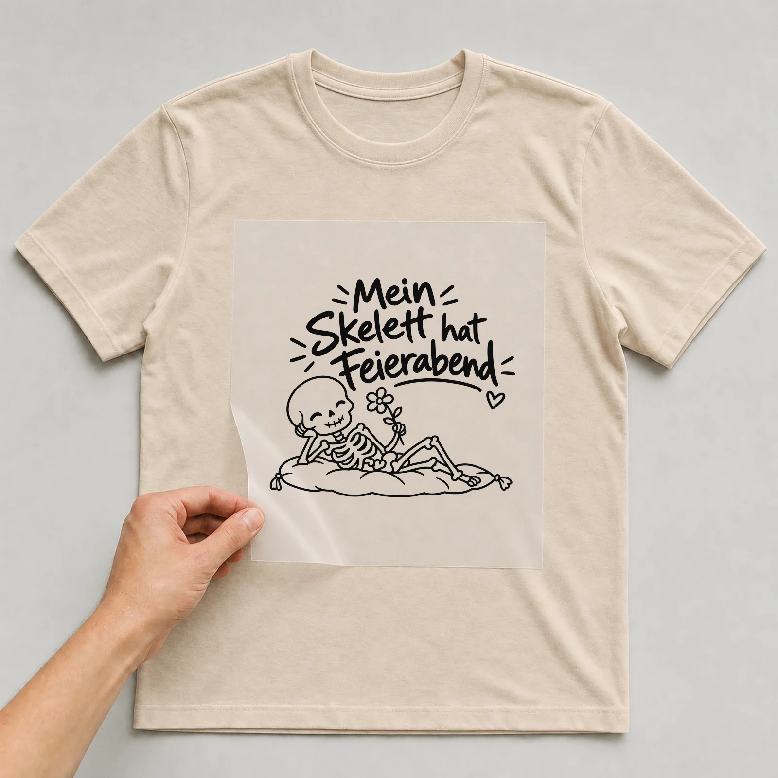 Bügelbild „Mein Skelett hat Feierabend“ auf beigem T-Shirt, Folie wird aufgelegt