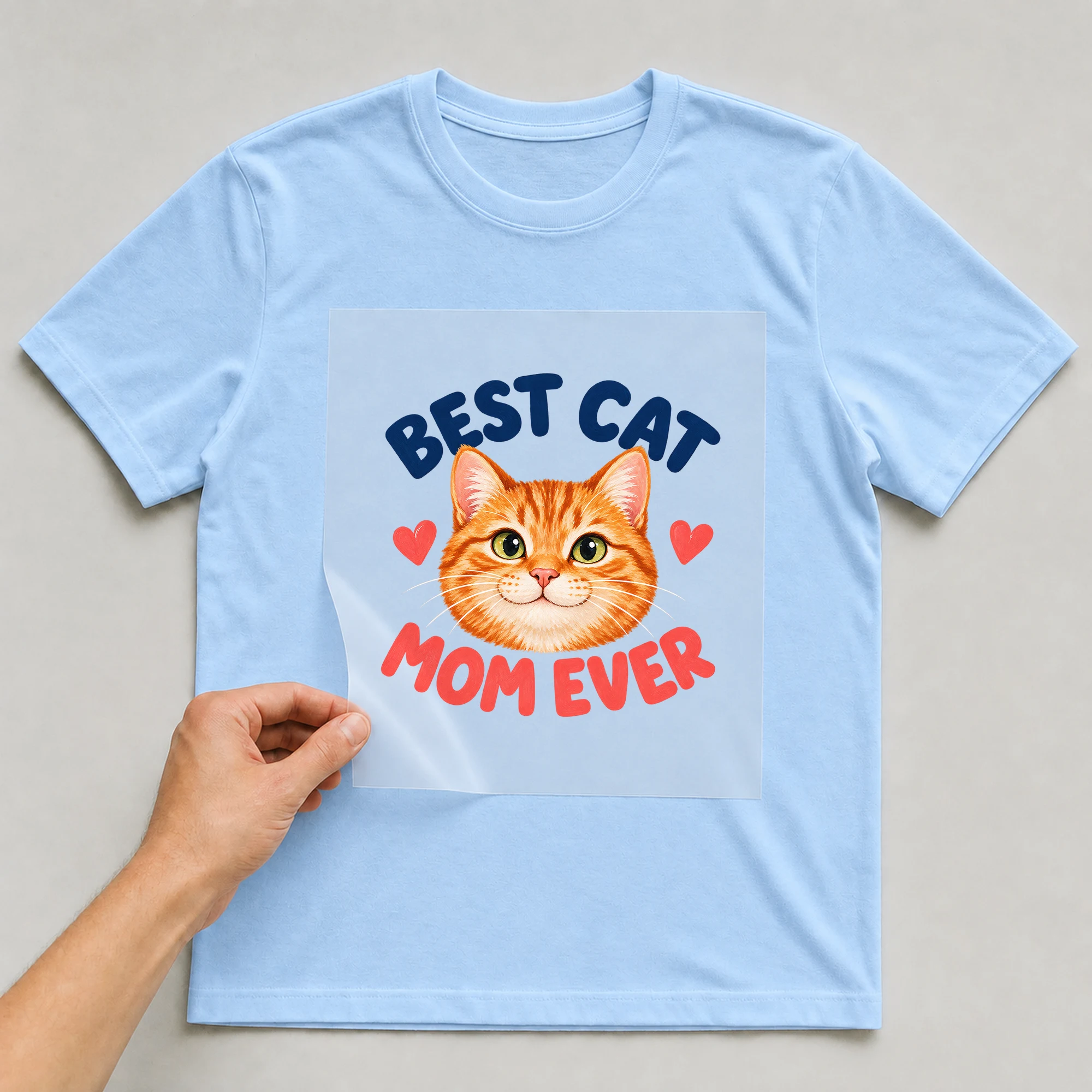 Bügelbild „Best Cat Mom Ever“ auf babyblauem T-Shirt, Folie wird aufgelegt